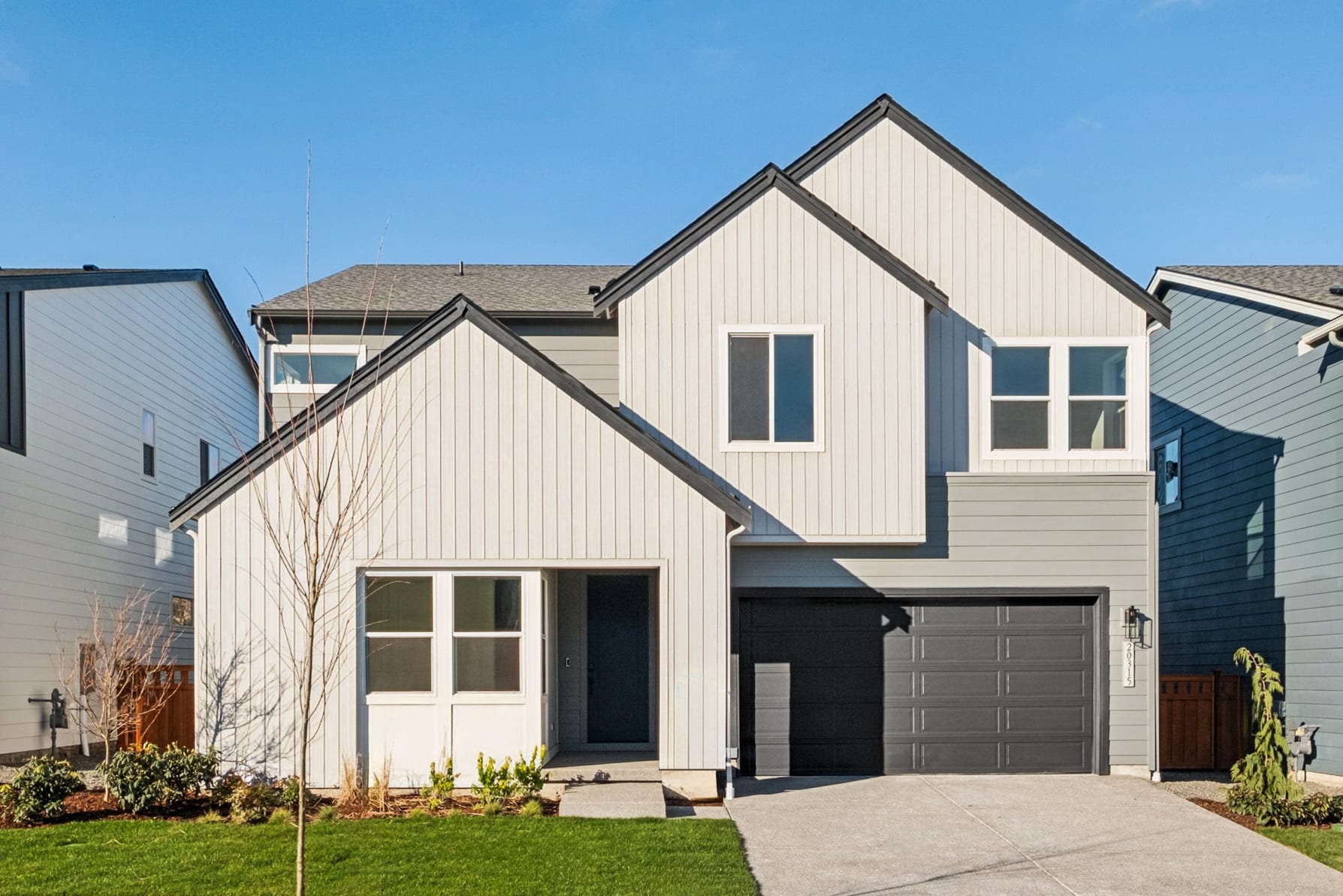A modern two-story house with a white exterior, a garage, and a well-maintained lawn in the foreground, set against a clear blue sky in the background.