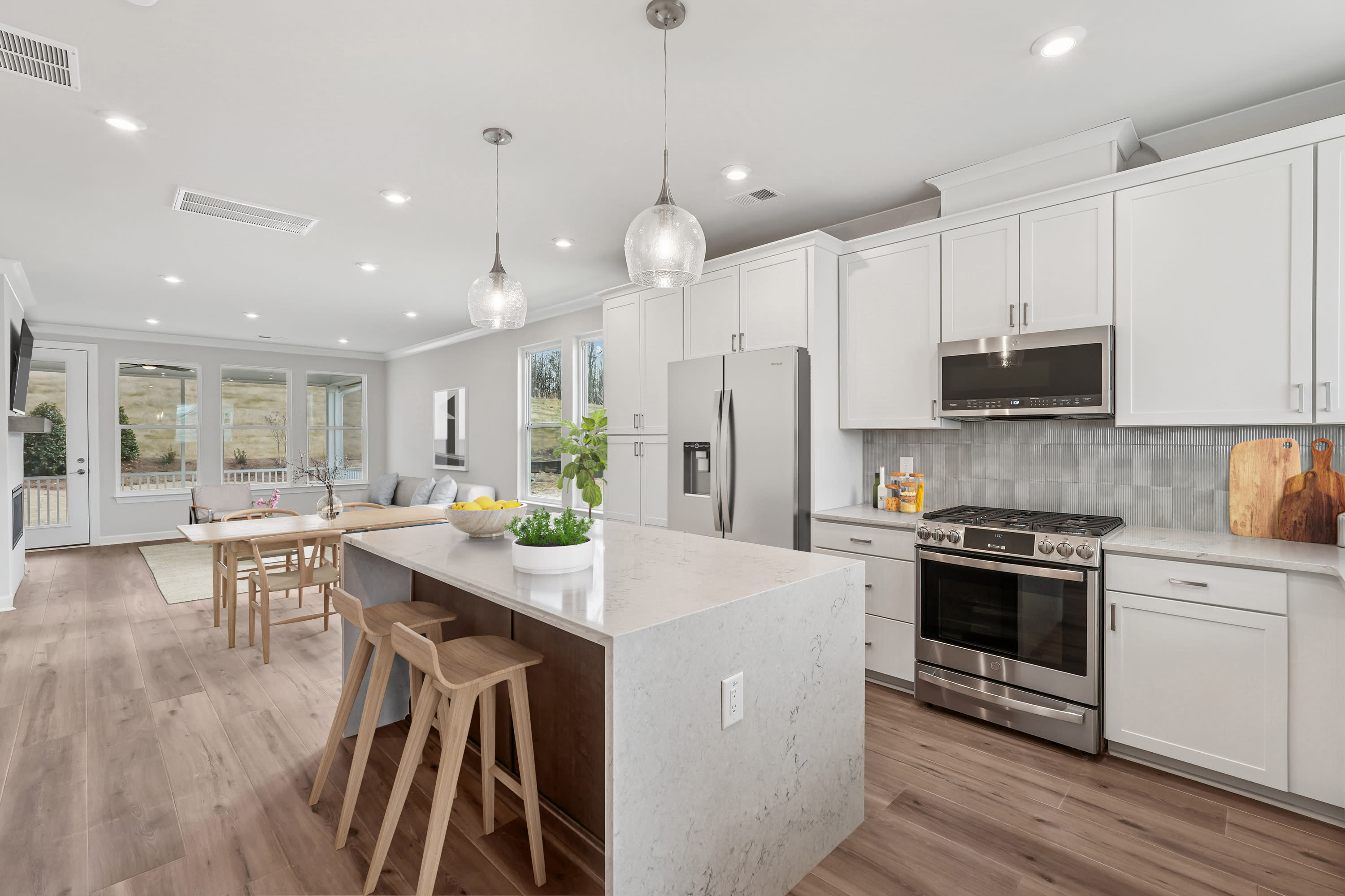 A modern, open-concept kitchen with white cabinets, stainless steel appliances, and a large island with bar stools, set against a backdrop of hardwood floors and pendant lighting.