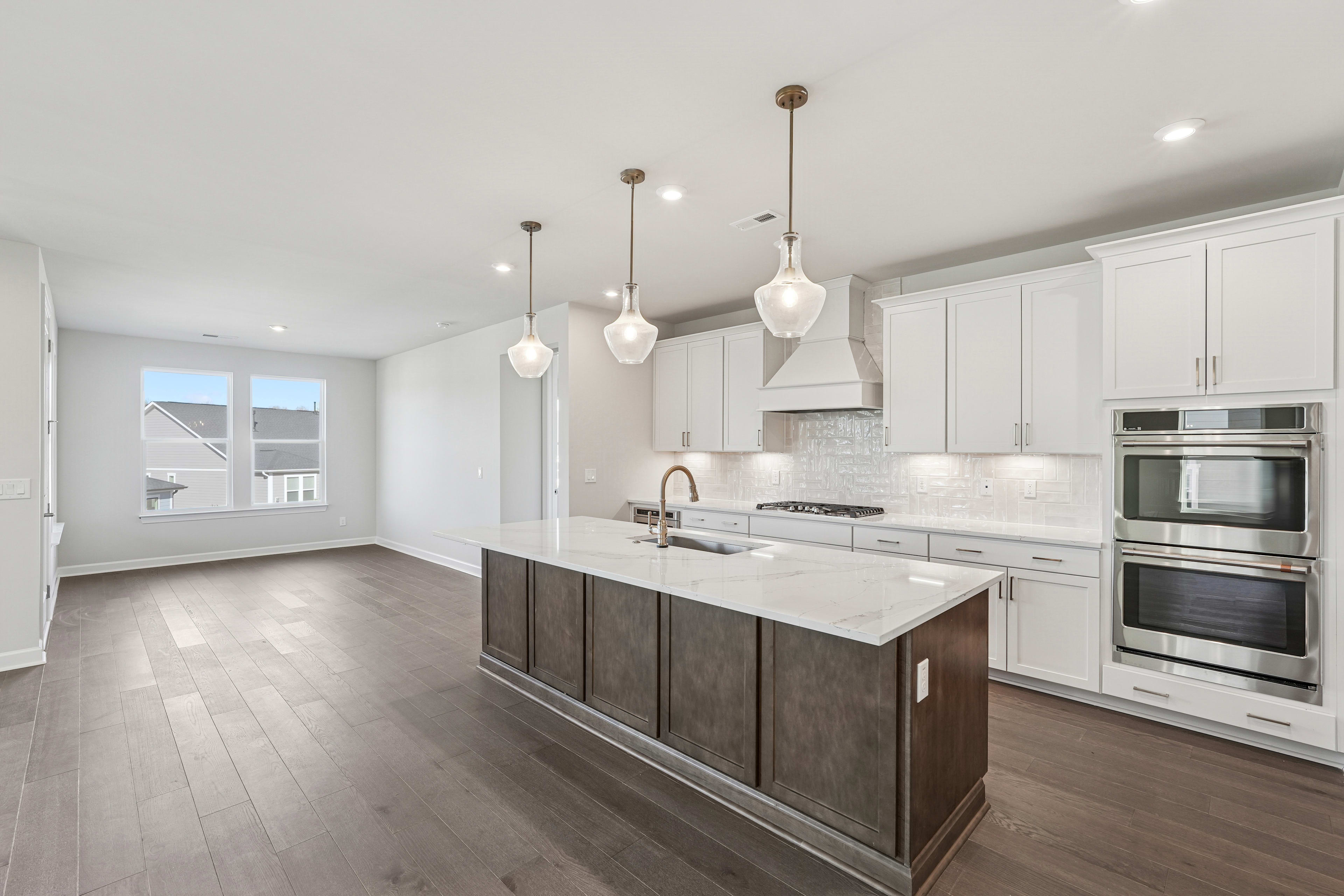 A modern, open-concept kitchen with white cabinets, a large island, and pendant lighting fixtures, set against a backdrop of hardwood floors and a bright, airy space.