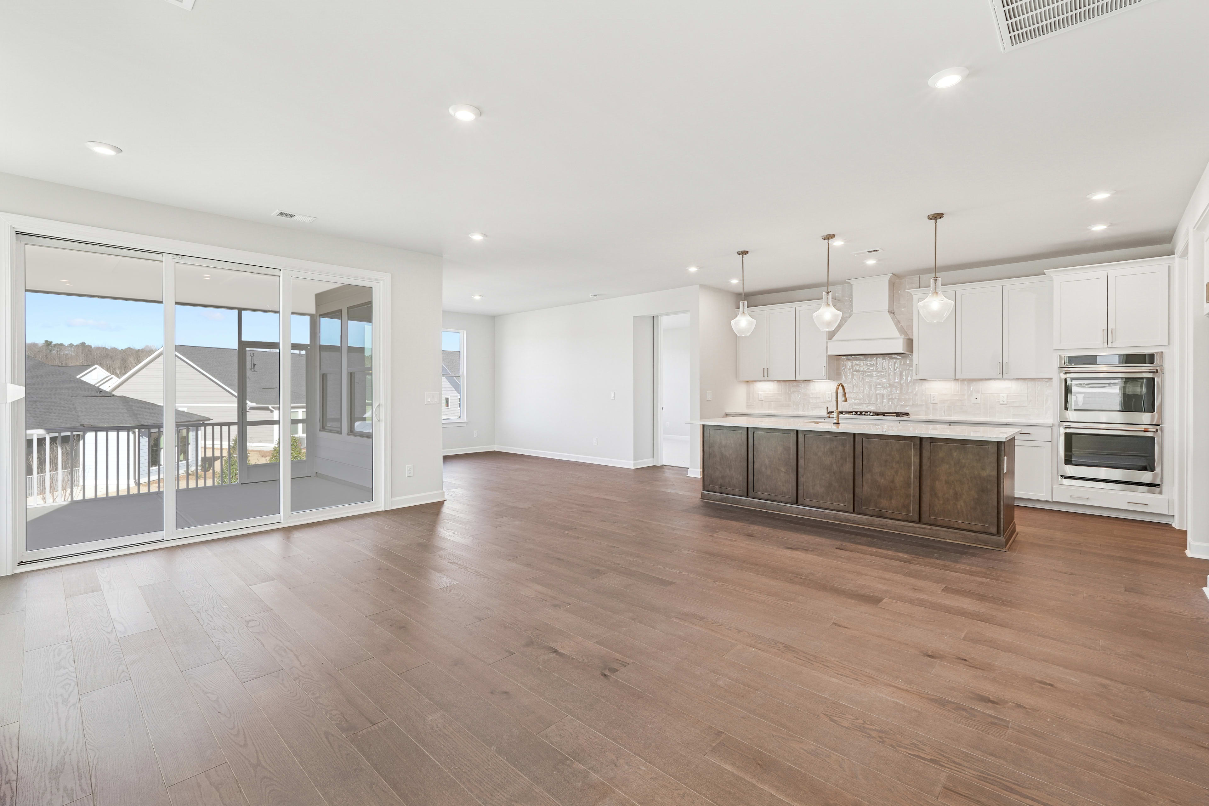 A spacious and modern kitchen with white cabinets, wooden floors, and large windows overlooking a balcony or patio area.