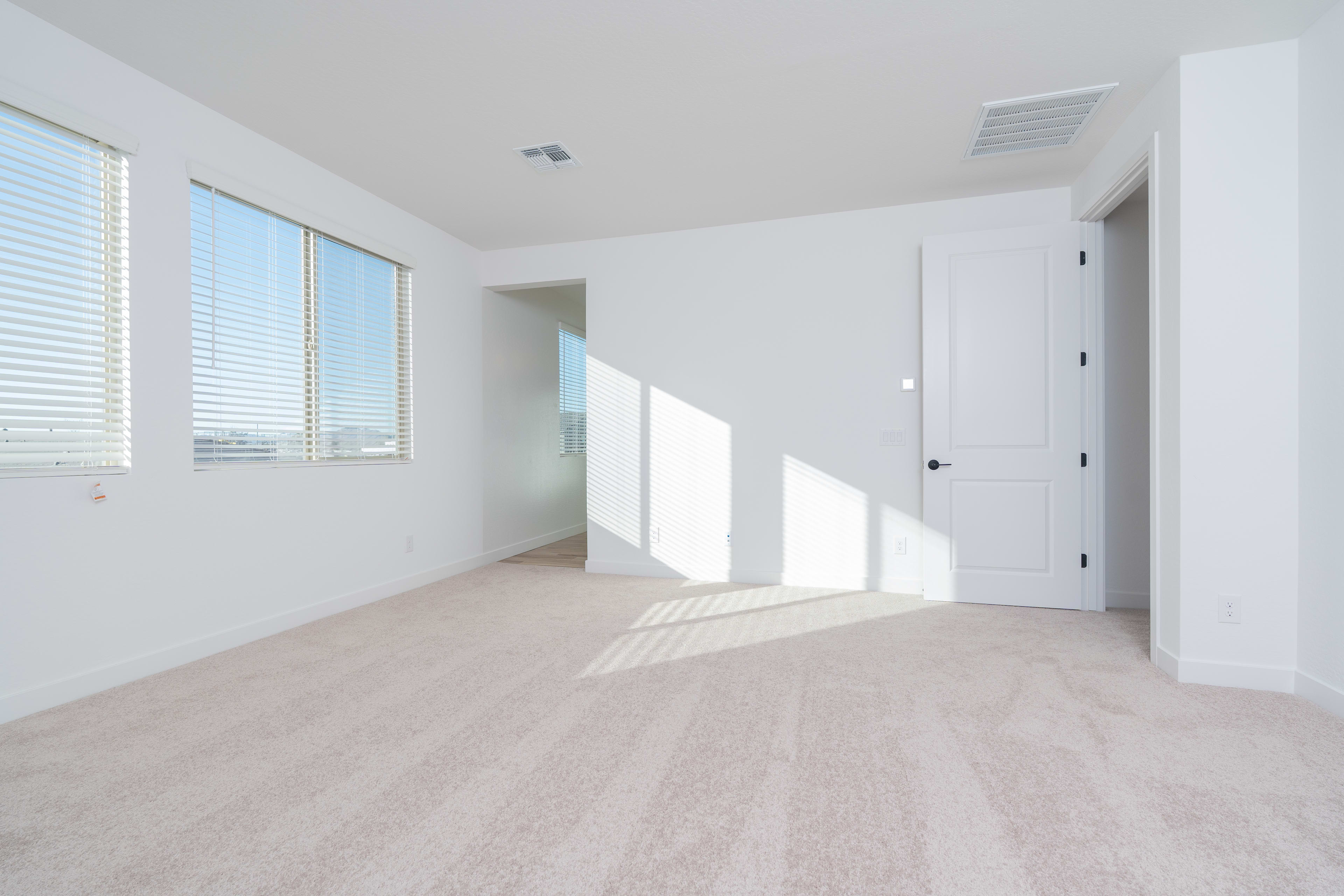 A bright, spacious room with large windows, white walls, and a light-colored hardwood floor. The room appears to be empty, creating a sense of openness and minimalism.