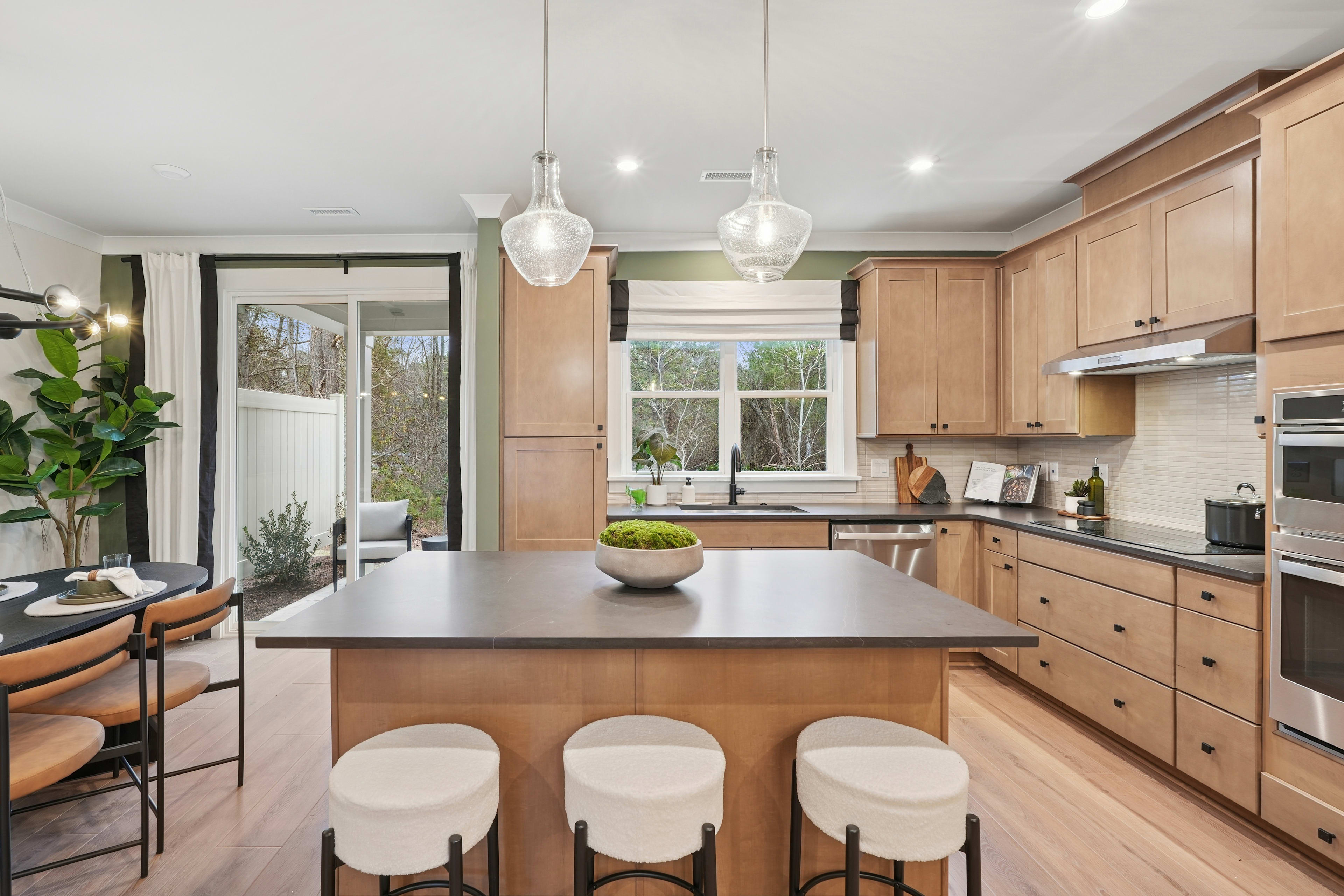 A modern and spacious kitchen with wooden cabinets, a large island with stools, and pendant lights illuminating the space.