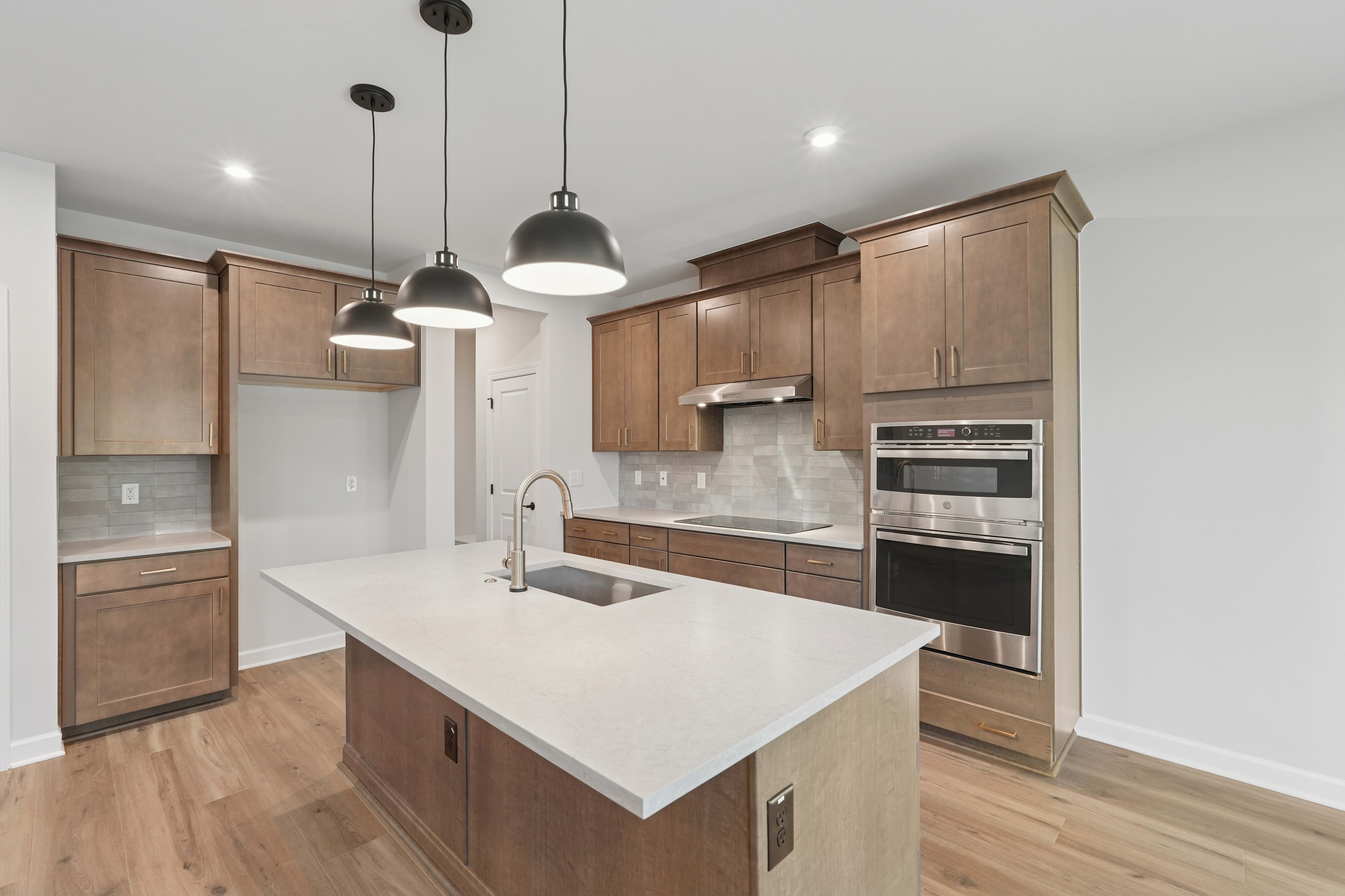 A modern, well-lit kitchen with light wood cabinets, a white countertop, and pendant lights hanging above the island.