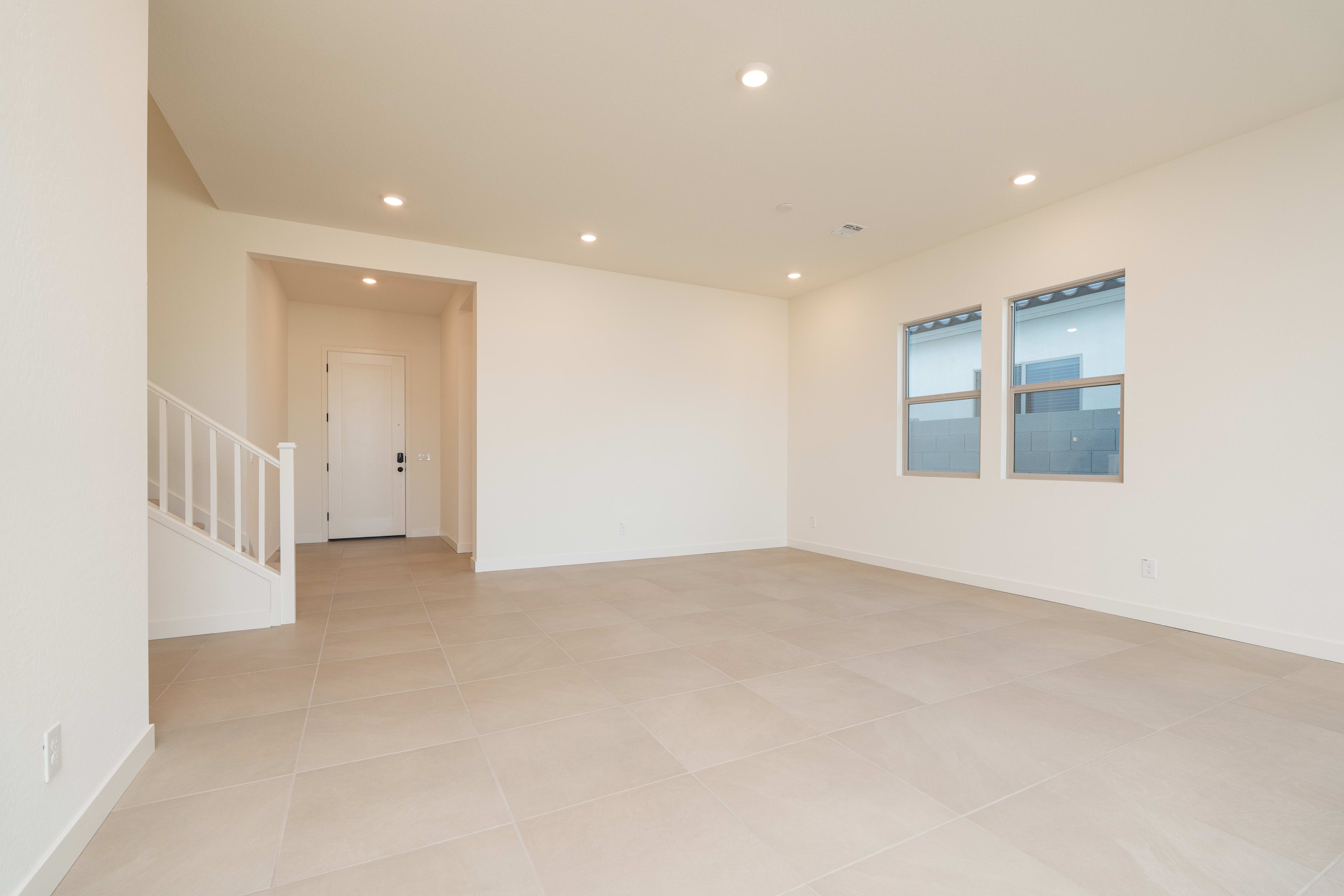 A spacious, minimalist room with white walls, a hardwood floor, and recessed lighting, featuring a doorway leading to another area.