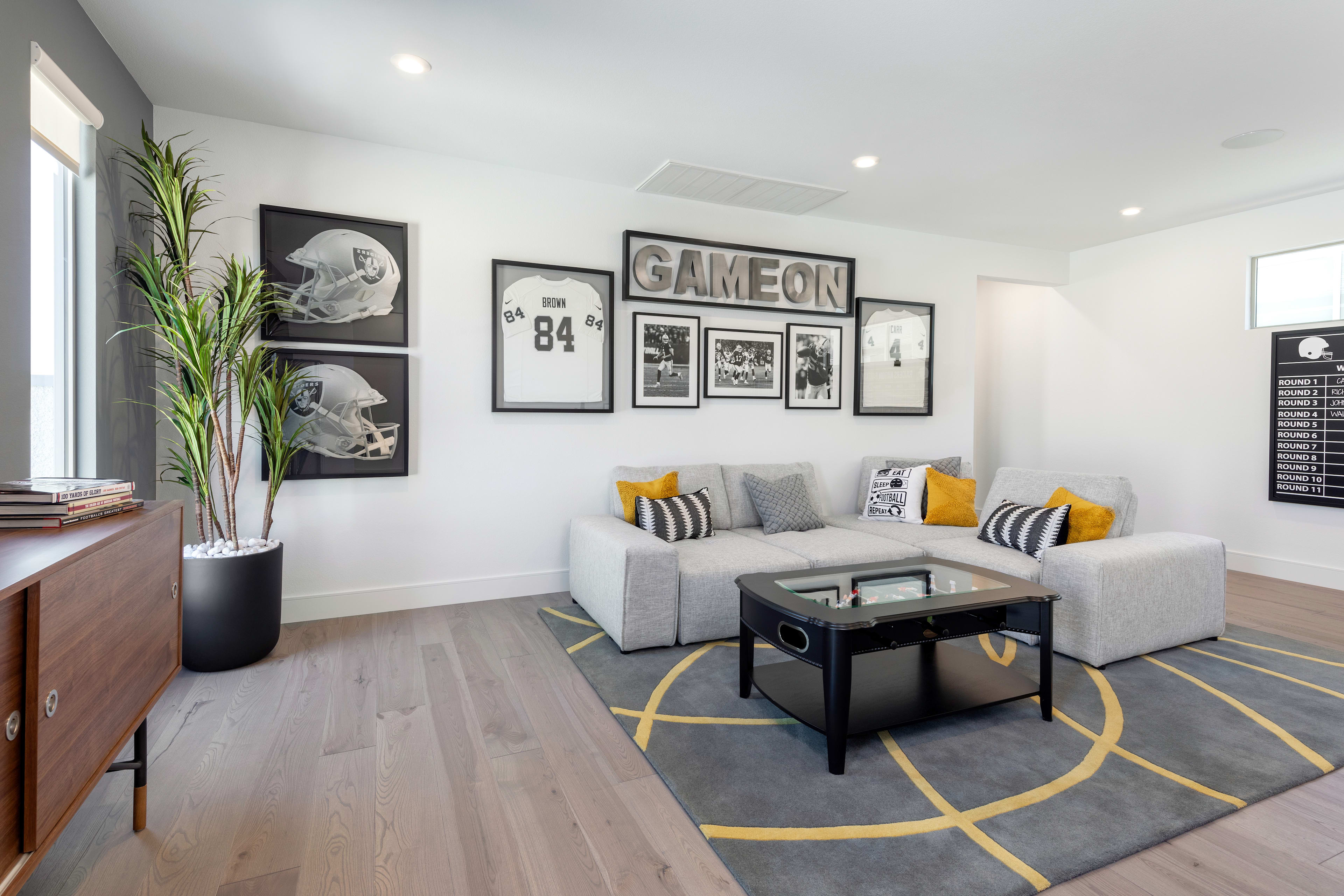 A modern and stylish living room with a gray sectional sofa, a black coffee table, and framed artwork on the walls, including a "Game On '84" sign, creating a cozy and inviting atmosphere.