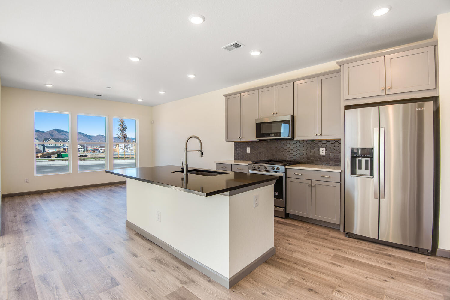 A modern, open-concept kitchen with gray cabinets, stainless steel appliances, and a large window overlooking a scenic outdoor landscape.