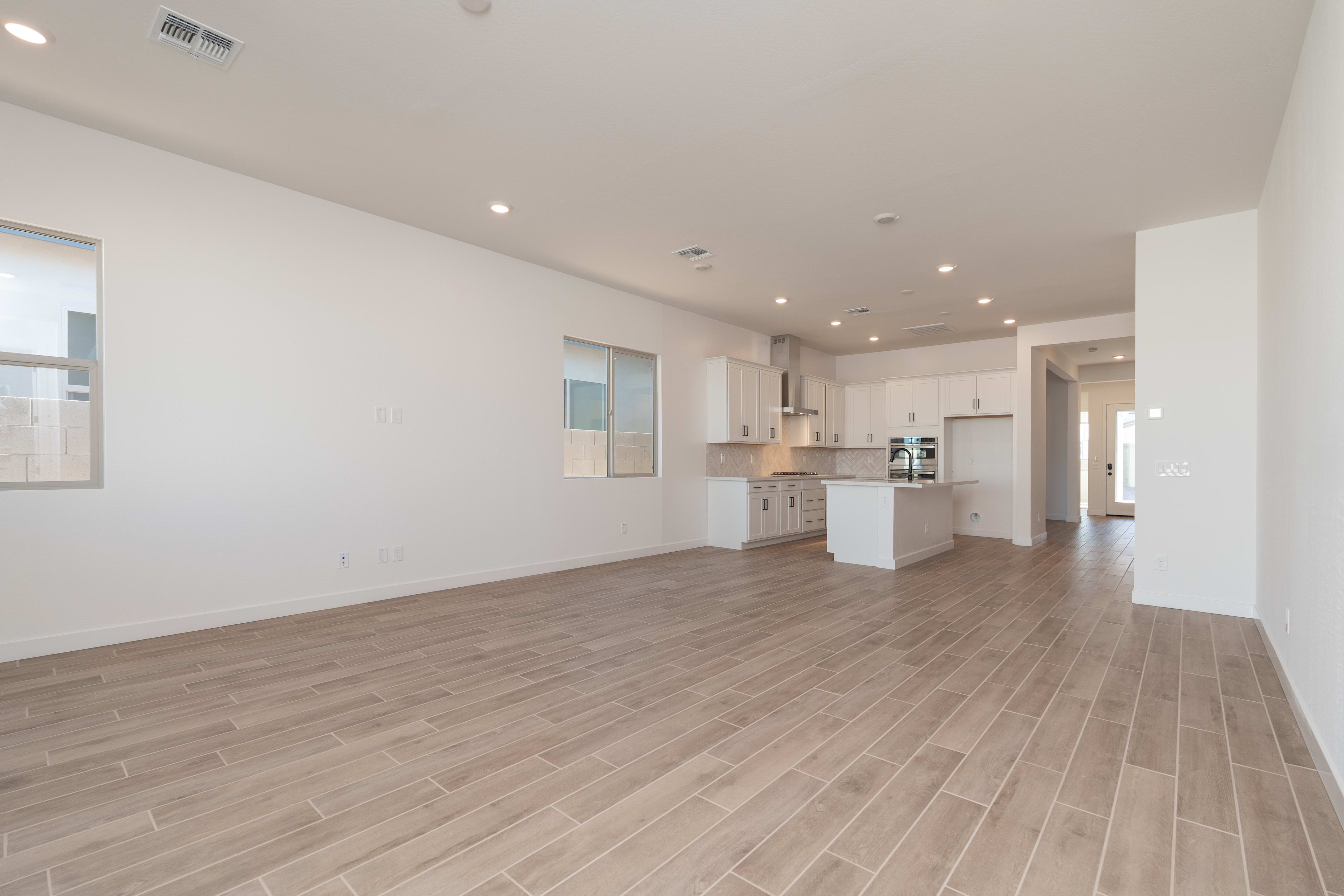 A spacious, open-concept living area with a kitchen visible in the background, featuring hardwood-style flooring and a clean, minimalist design.