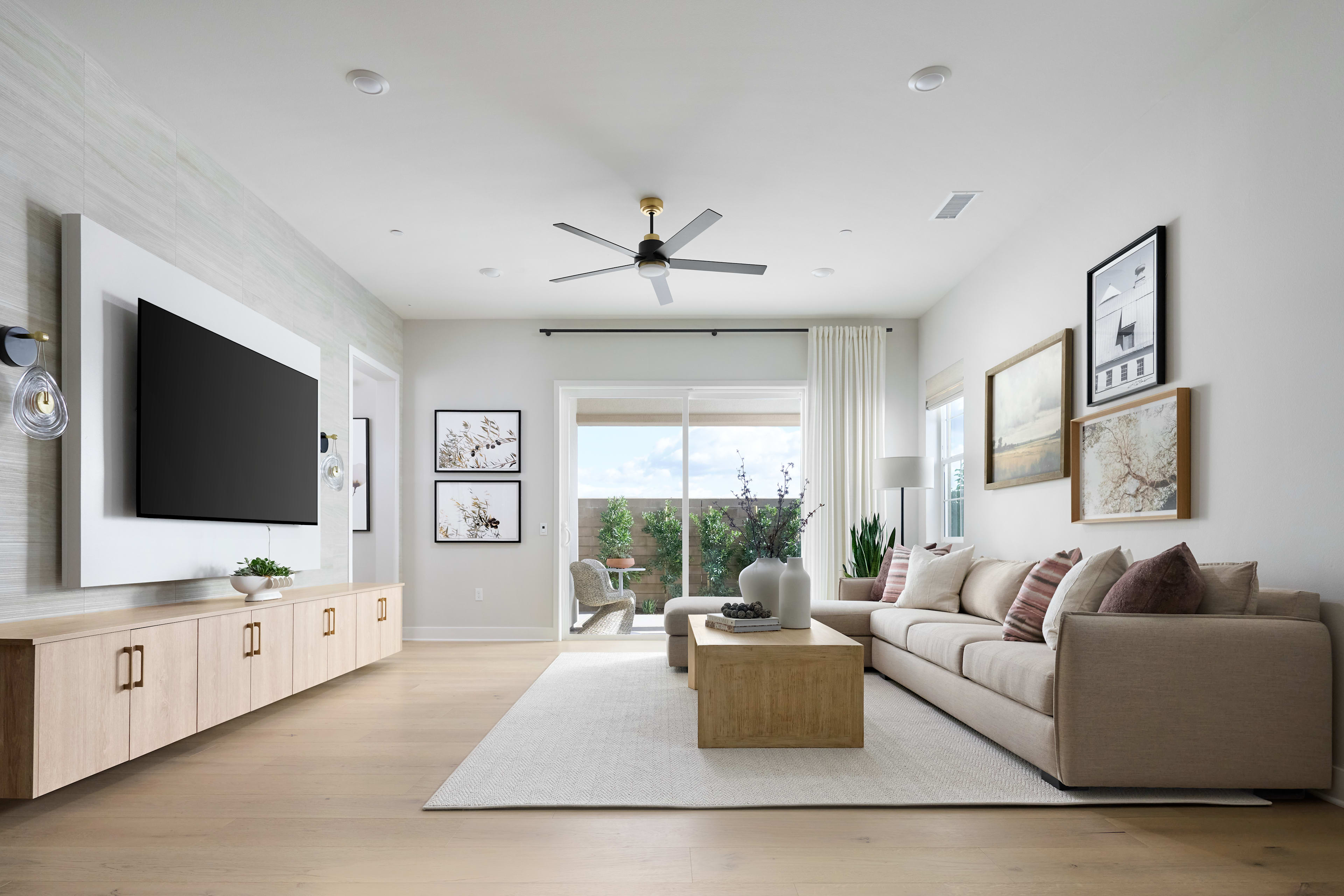 A modern and minimalist living room with a large beige sofa, a wooden coffee table, and a wall-mounted TV surrounded by framed artwork and potted plants, creating a cozy and inviting atmosphere.