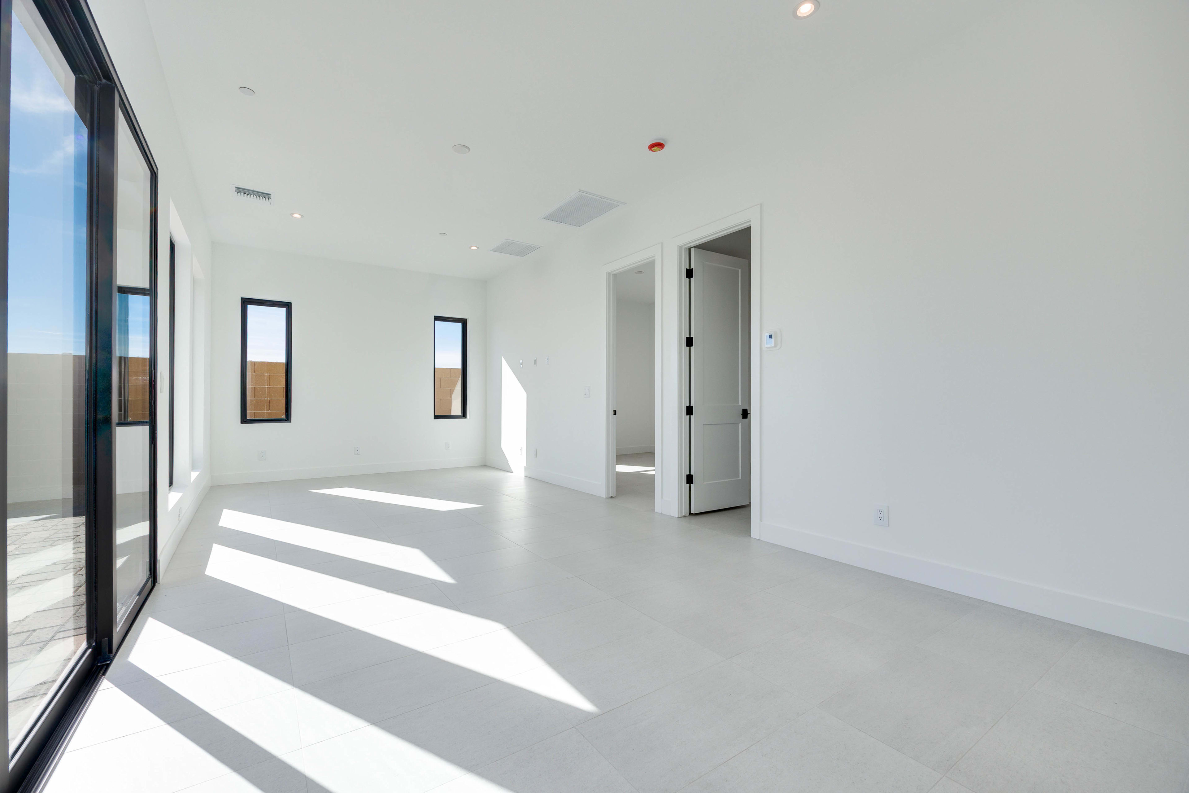 A spacious, minimalist interior with large windows, white walls, and a smooth, light-colored floor. The room appears to be well-lit, with natural light streaming in through the windows.