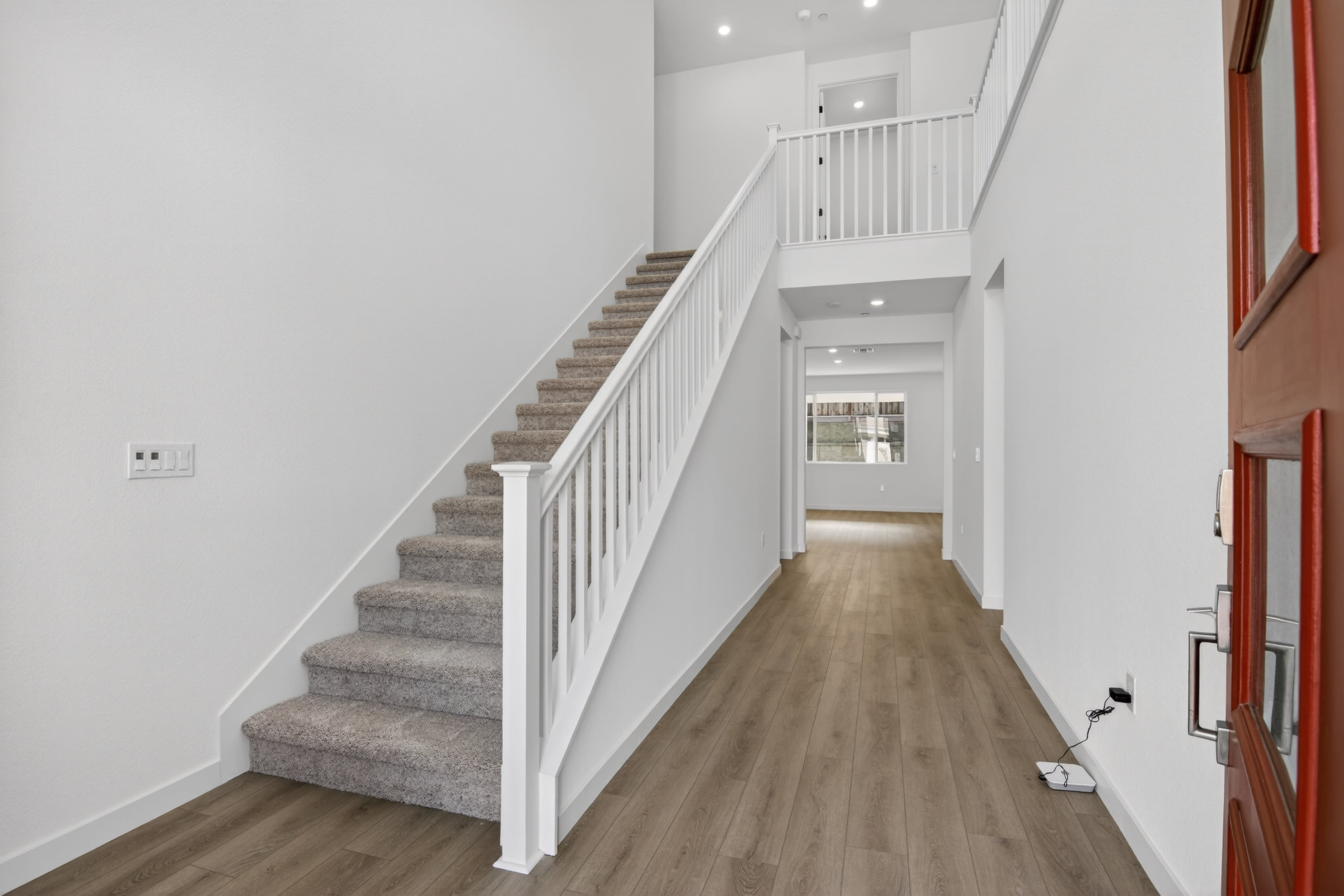 A bright and spacious hallway with a staircase leading up, featuring a wooden floor and white walls.