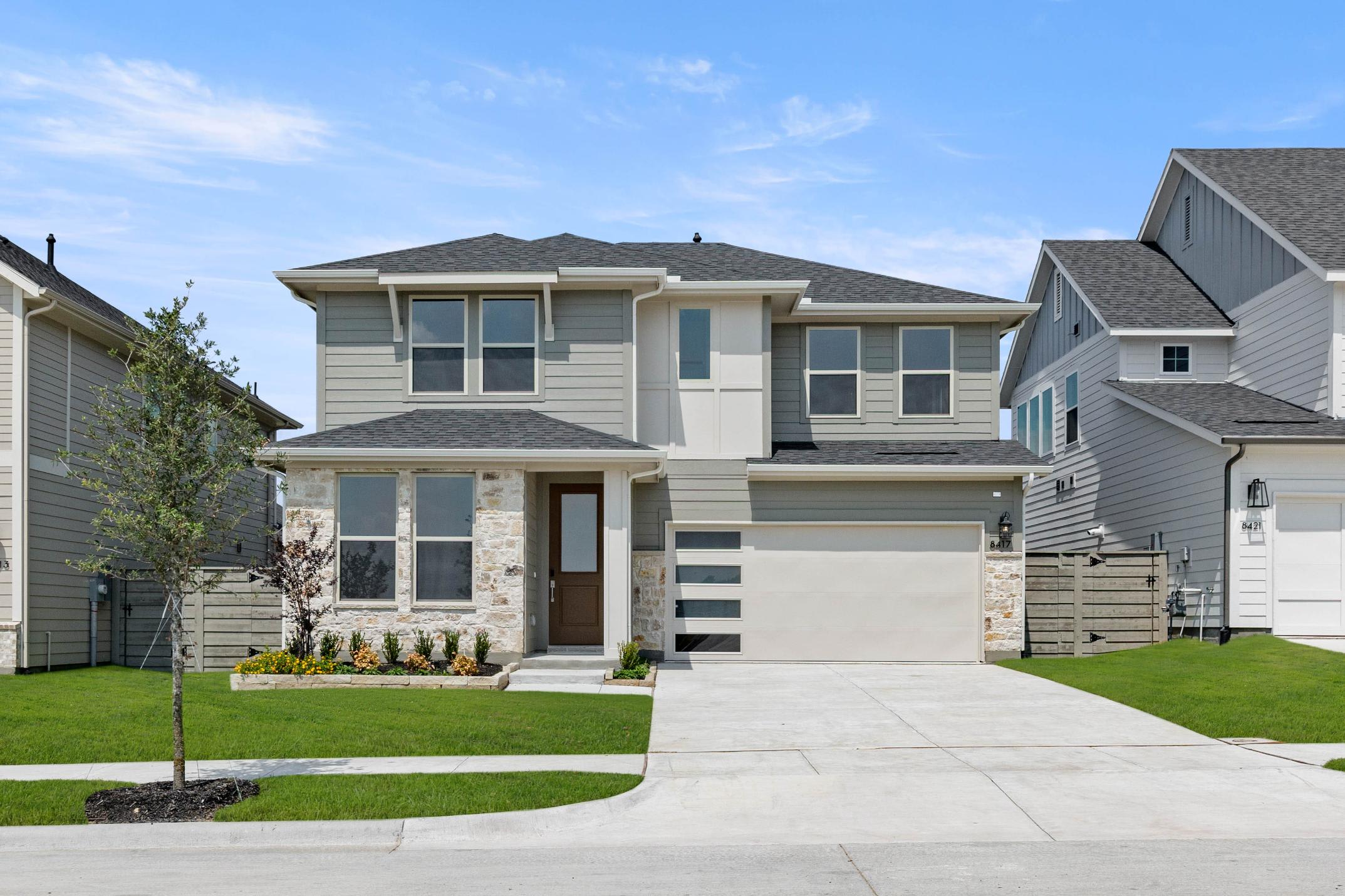 A two-story residential house with a well-manicured lawn, surrounded by other similar houses in a suburban neighborhood.