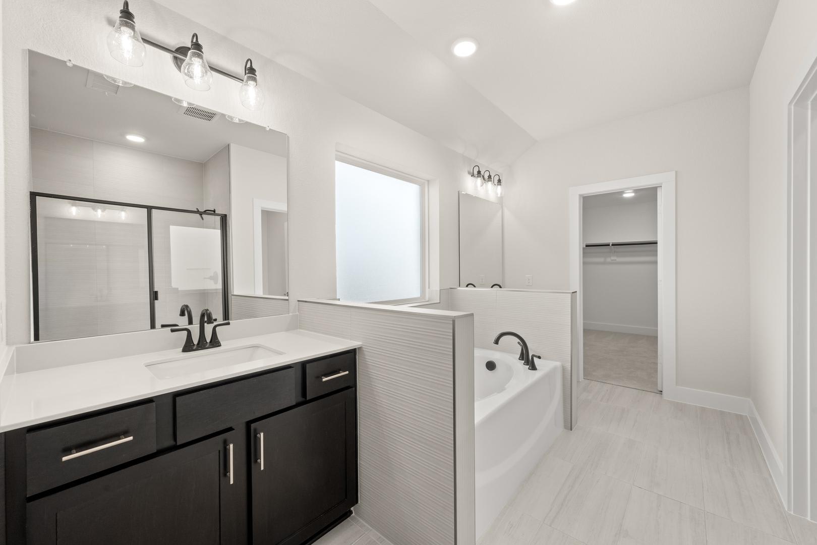 A modern, minimalist bathroom with a double vanity, white countertops, and dark cabinets, featuring a large mirror and recessed lighting.