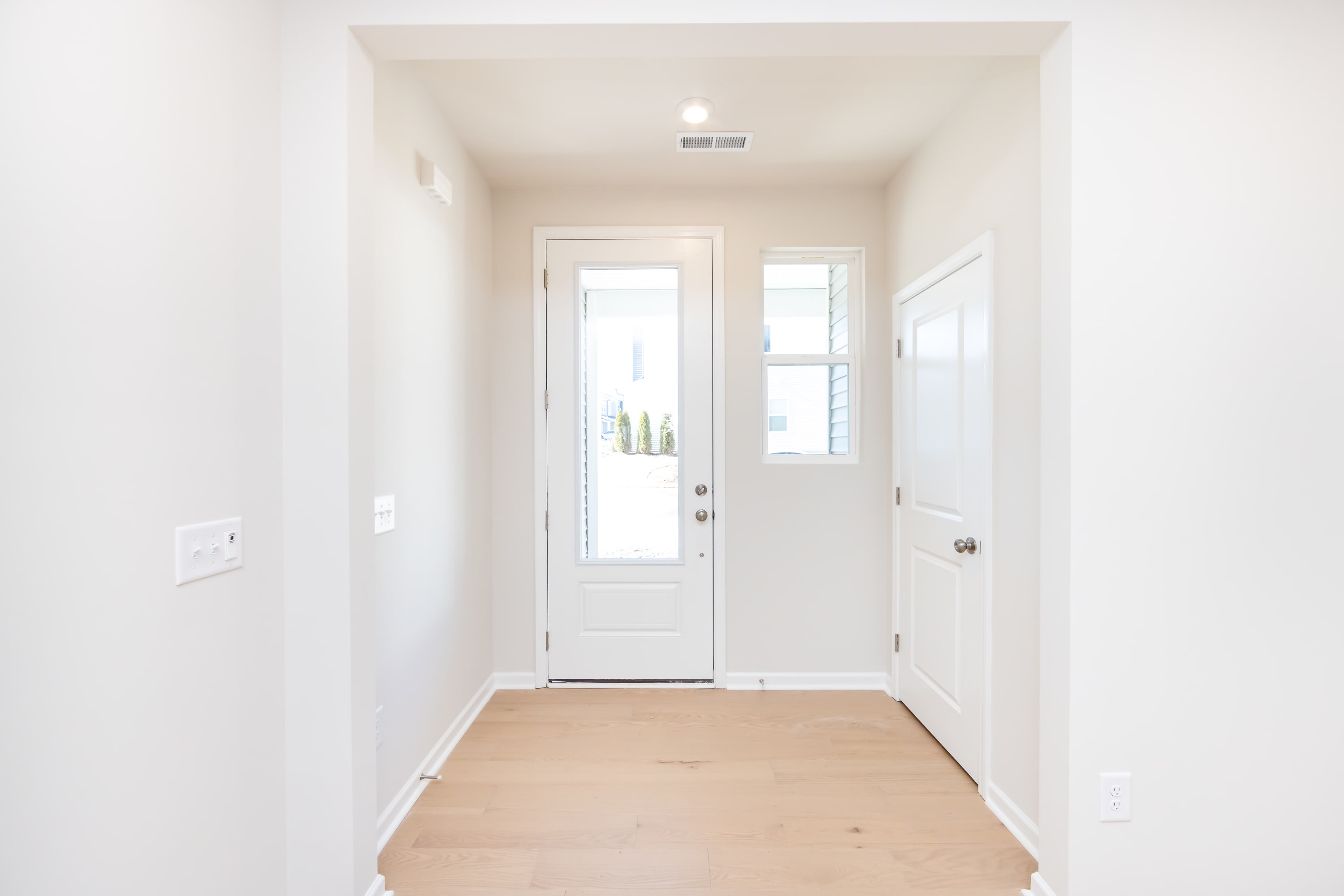 A bright, minimalist entryway with a white door, walls, and hardwood flooring, creating a clean and inviting atmosphere.