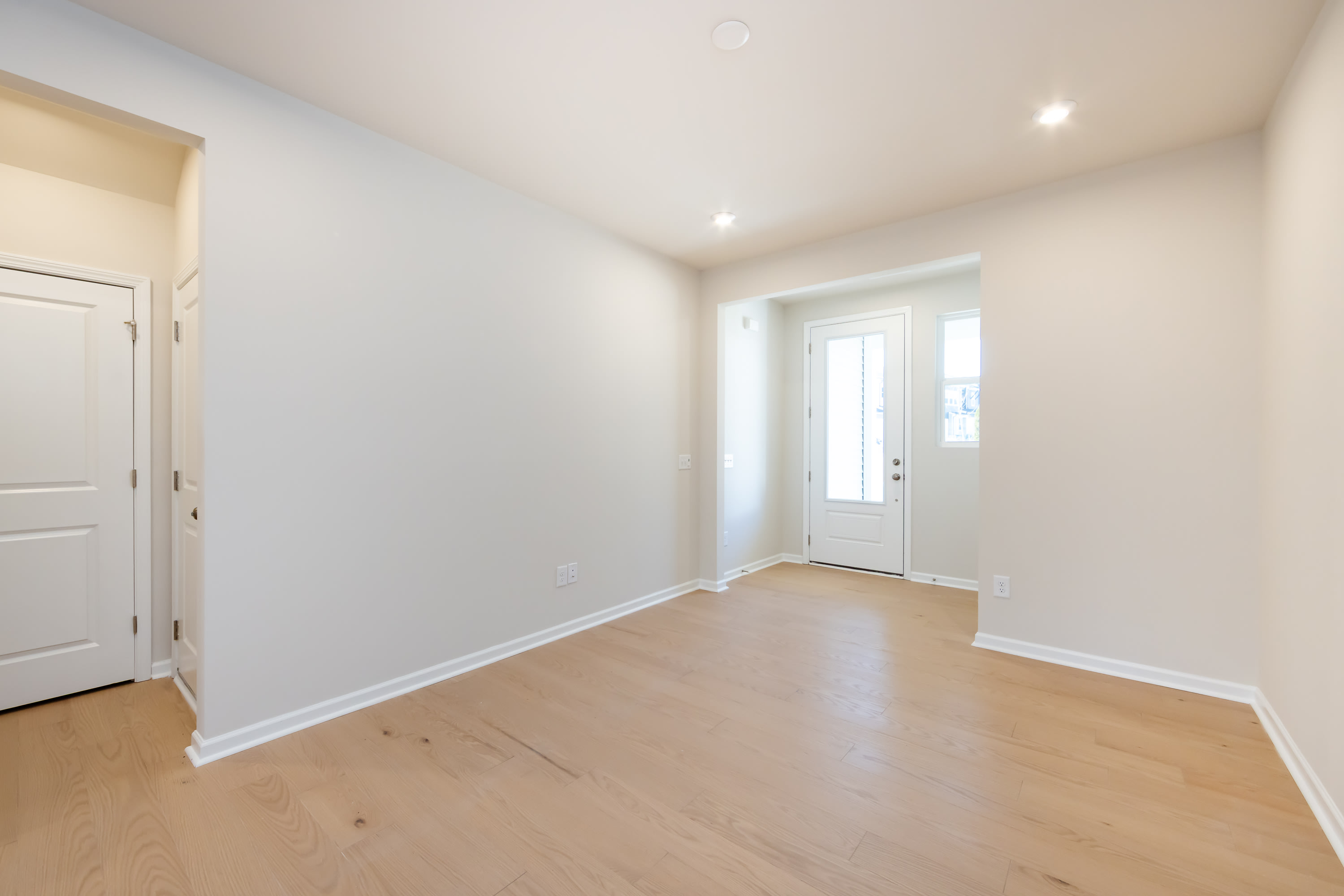 A bright, spacious room with white walls, a wooden floor, and a door leading to the exterior.