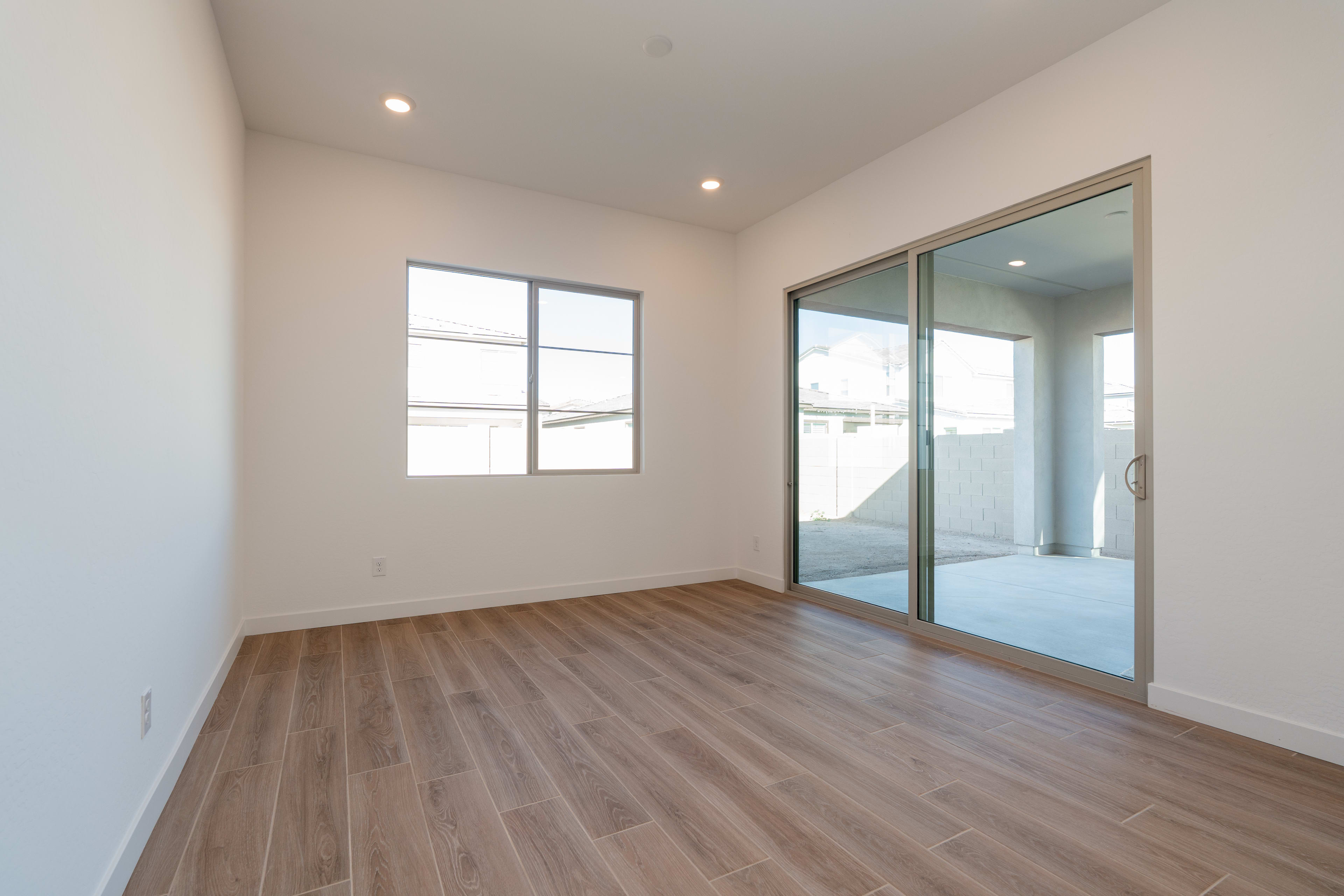 A spacious, well-lit room with a wooden floor, a large window, and a sliding glass door leading to an outdoor area.