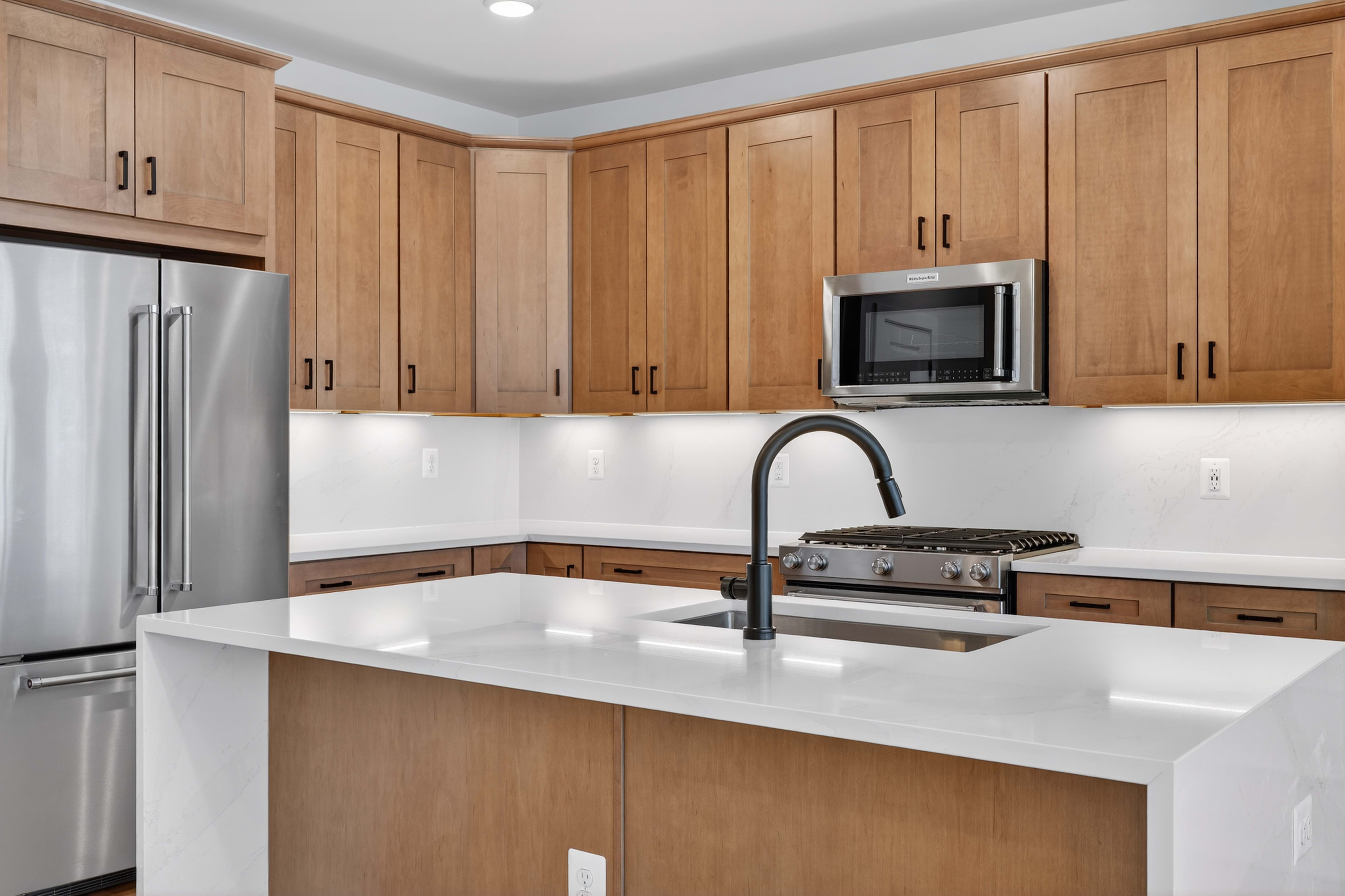 A modern kitchen with light wood cabinets, a white countertop, and stainless steel appliances.