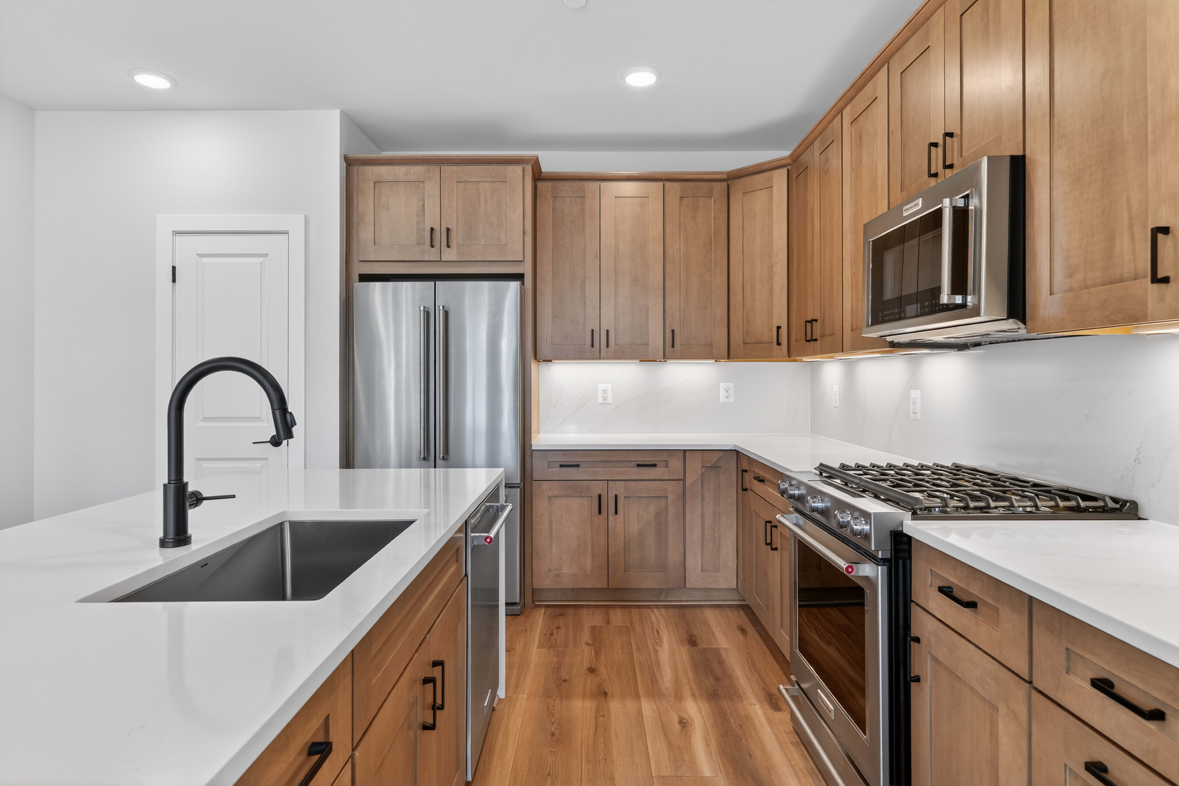 A modern and well-equipped kitchen with light wood cabinets, stainless steel appliances, and a sleek white countertop.