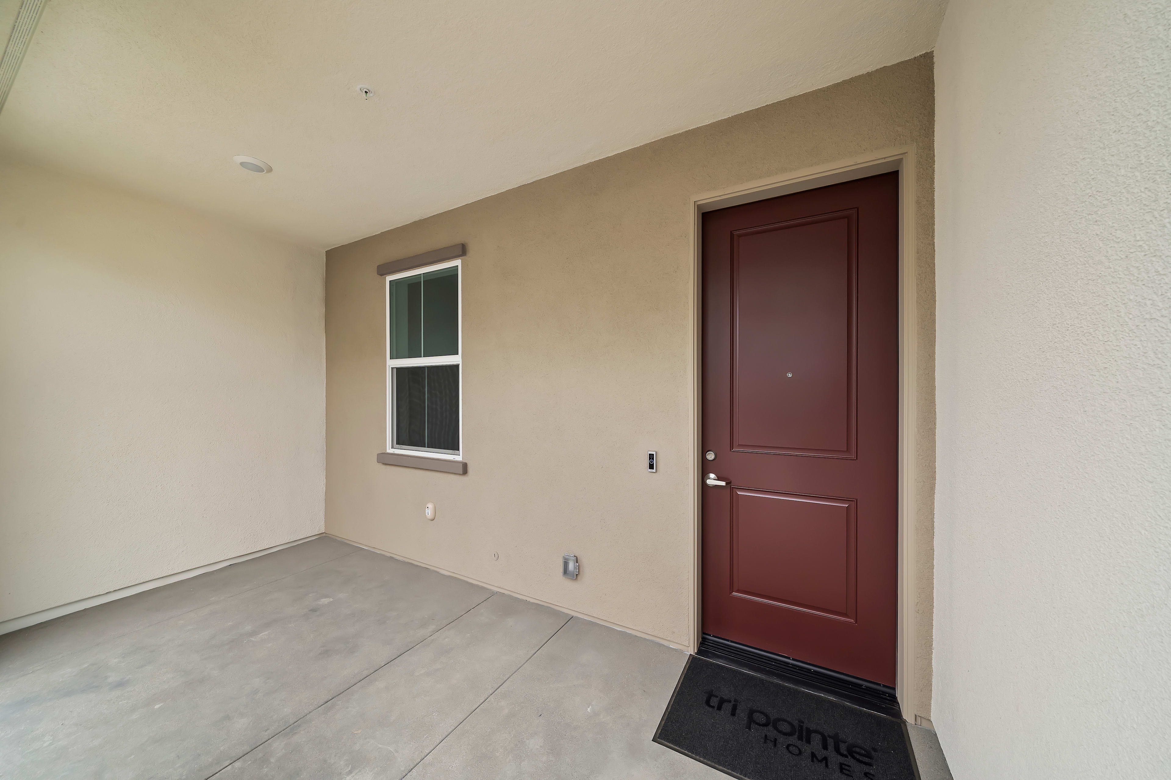 A simple, minimalist room with a wooden door and a window, featuring a plain, light-colored wall and a smooth, tiled floor.