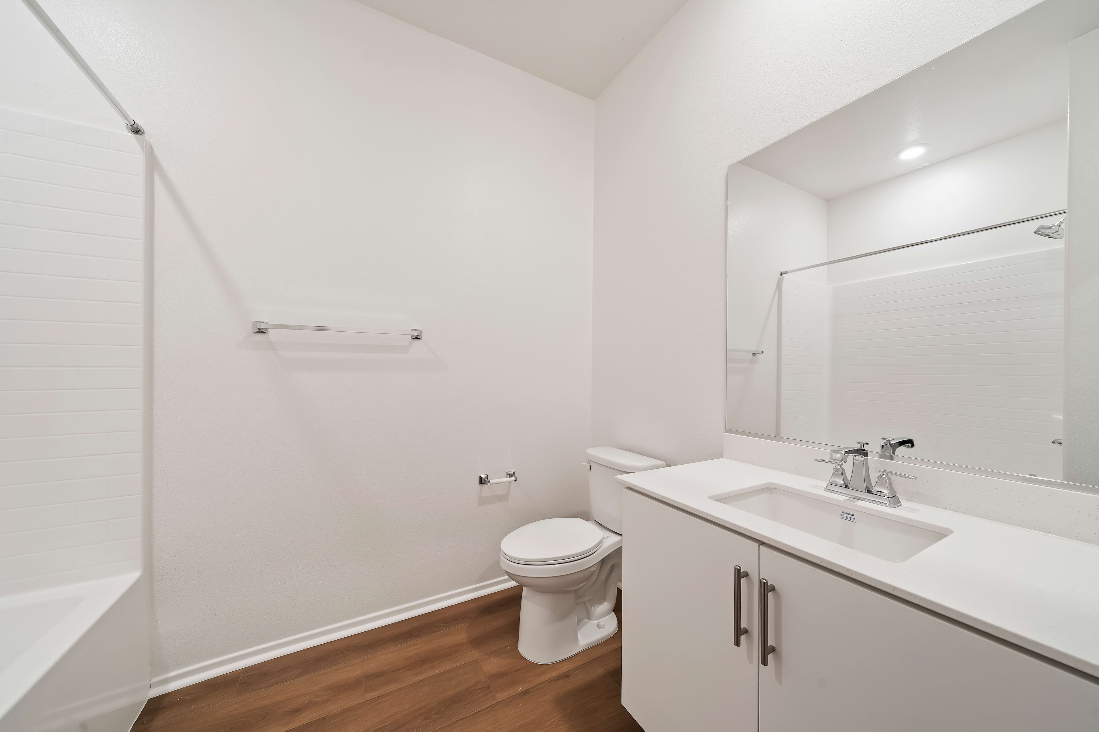 A modern, minimalist bathroom with a white vanity, toilet, and hardwood flooring.