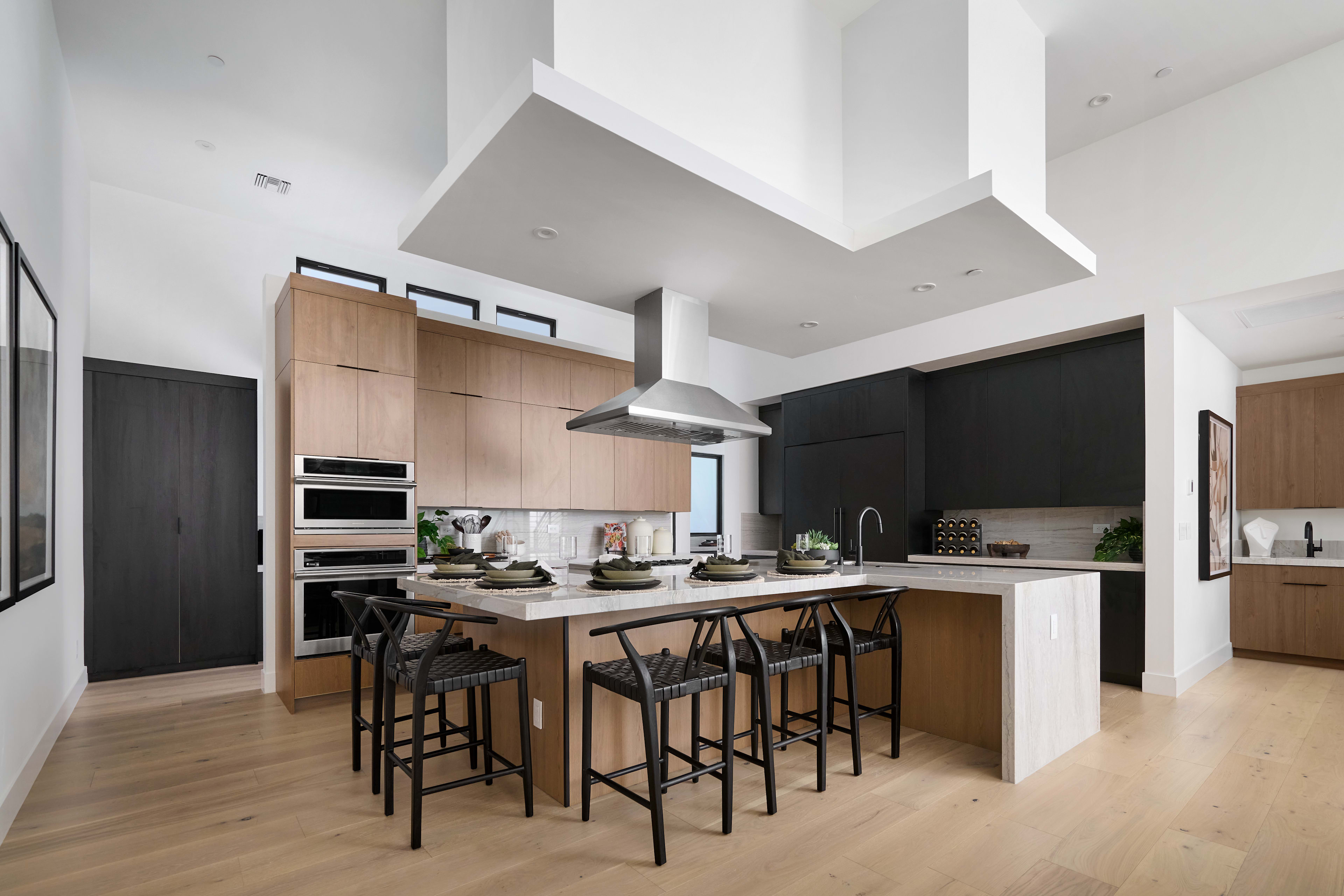 A modern, open-concept kitchen with a large island, wooden cabinetry, and high-ceilinged space featuring recessed lighting.