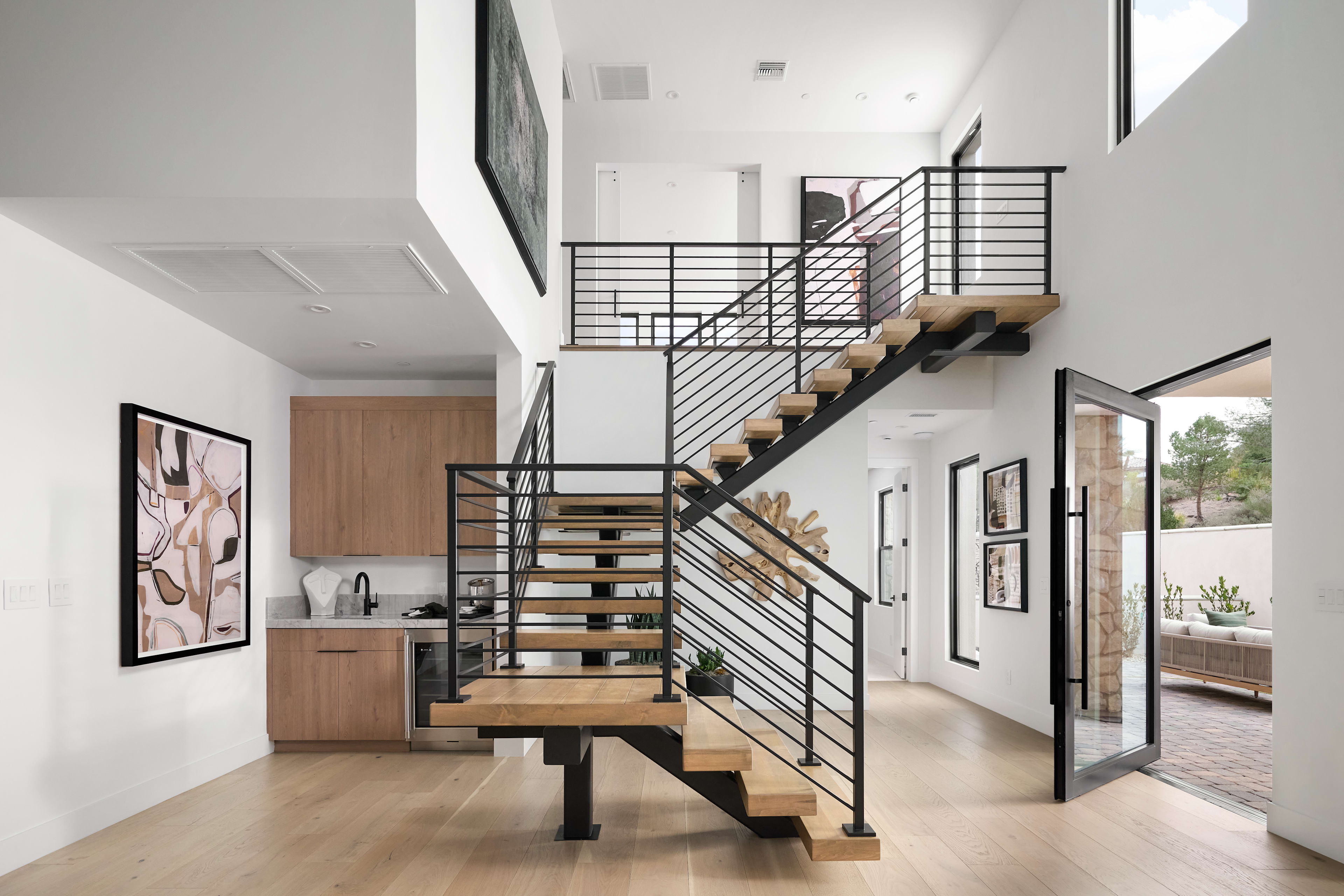 A modern, open-concept interior with a sleek, metal staircase leading up to a second level, surrounded by white walls, wooden floors, and framed artwork.