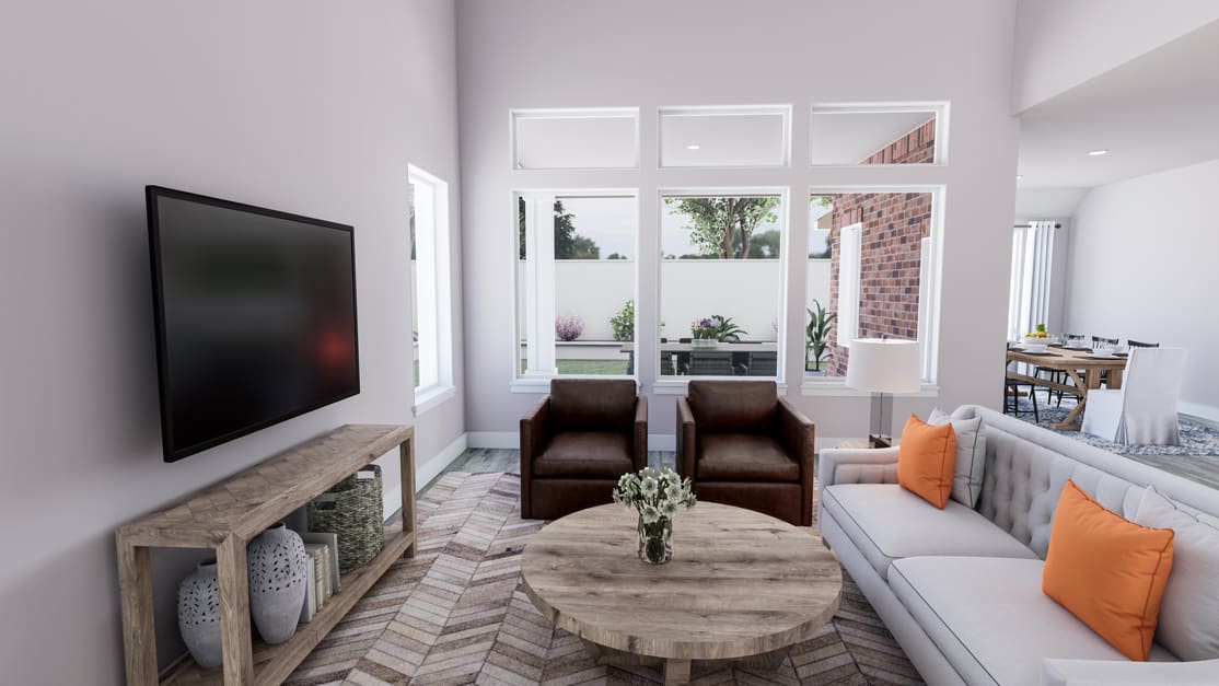 A cozy and modern living room with a large TV, two brown leather chairs, a wooden coffee table, and a gray sectional sofa with orange accent pillows. The room features large windows that let in natural light and provide a view of the outdoor greenery.