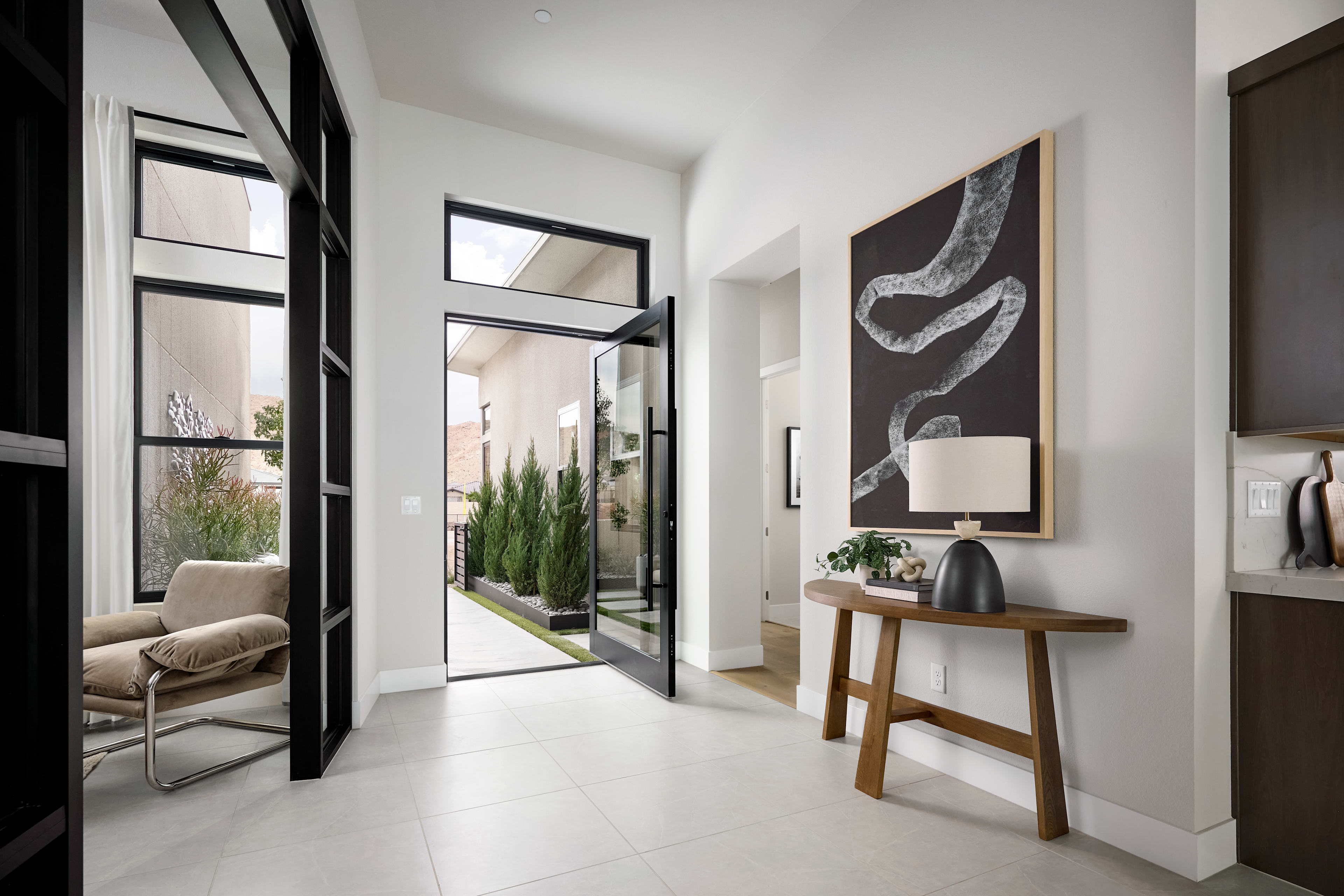 A modern and minimalist entryway with a wooden console table, a large abstract artwork, and a view of a small courtyard garden through the glass doors.