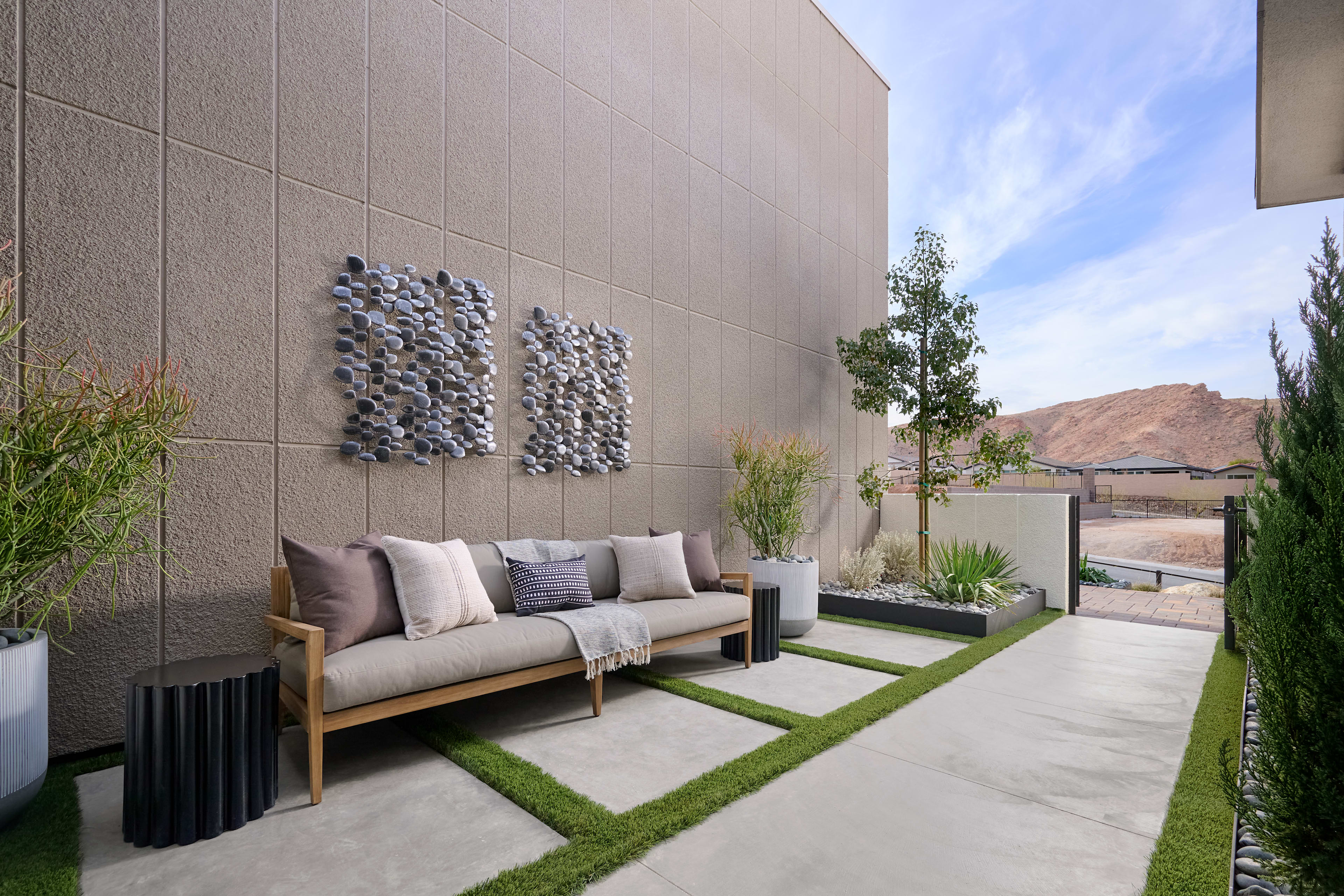 A modern outdoor seating area with a couch, decorative wall panels, and a grassy path leading to a scenic background.