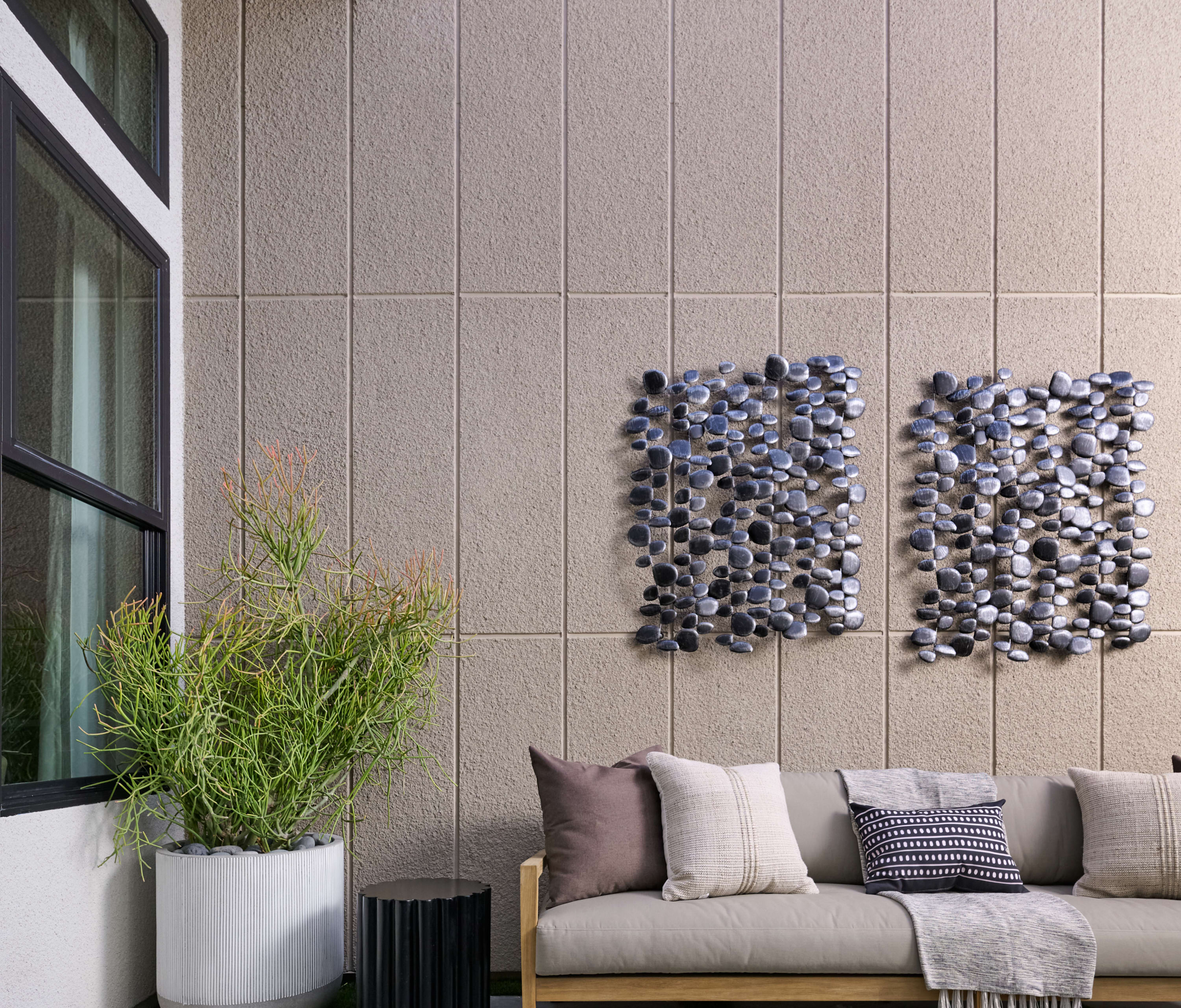 A modern and minimalist outdoor living space with a couch, potted plants, and a textured wall feature.