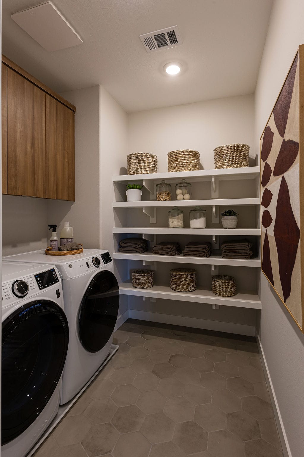 A modern and organized laundry room with a washing machine, shelves filled with baskets and decor, and a minimalist design aesthetic.