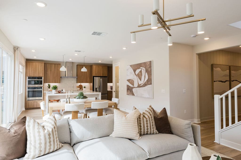 A modern and cozy open-concept living space with a comfortable sofa, a dining area, and a kitchen with wooden cabinetry and a unique light fixture.