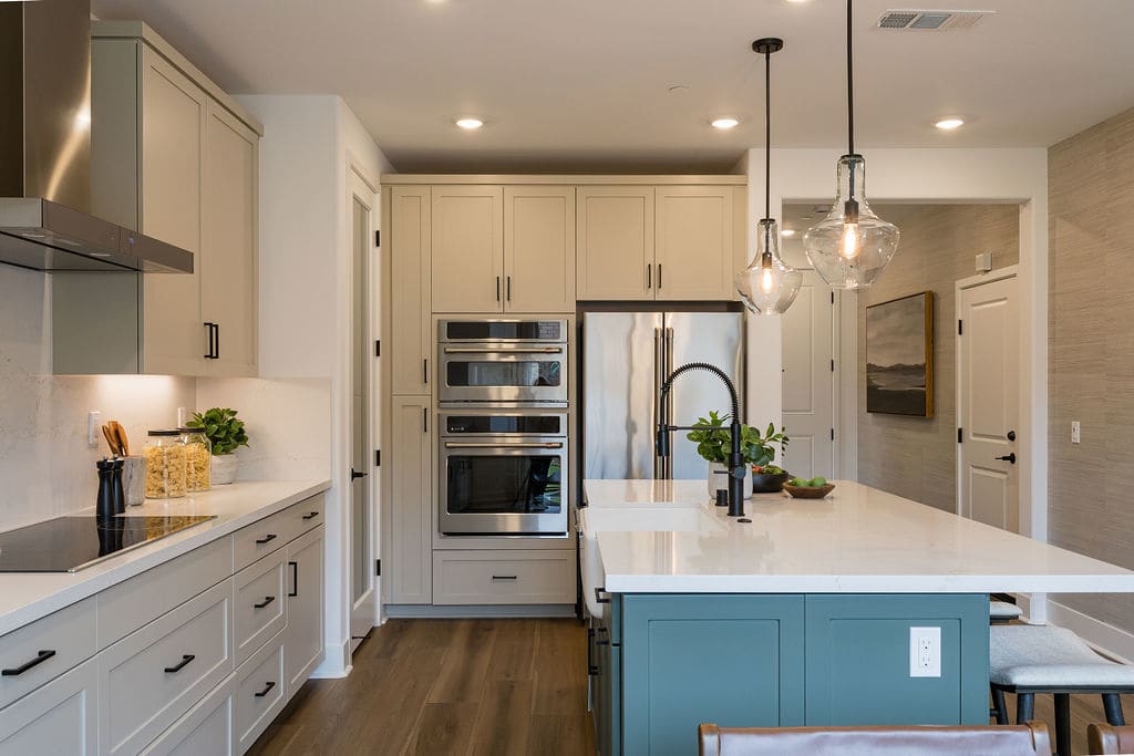 A modern, well-designed kitchen with white cabinets, a blue island, stainless steel appliances, and pendant lighting creating a warm and inviting atmosphere.