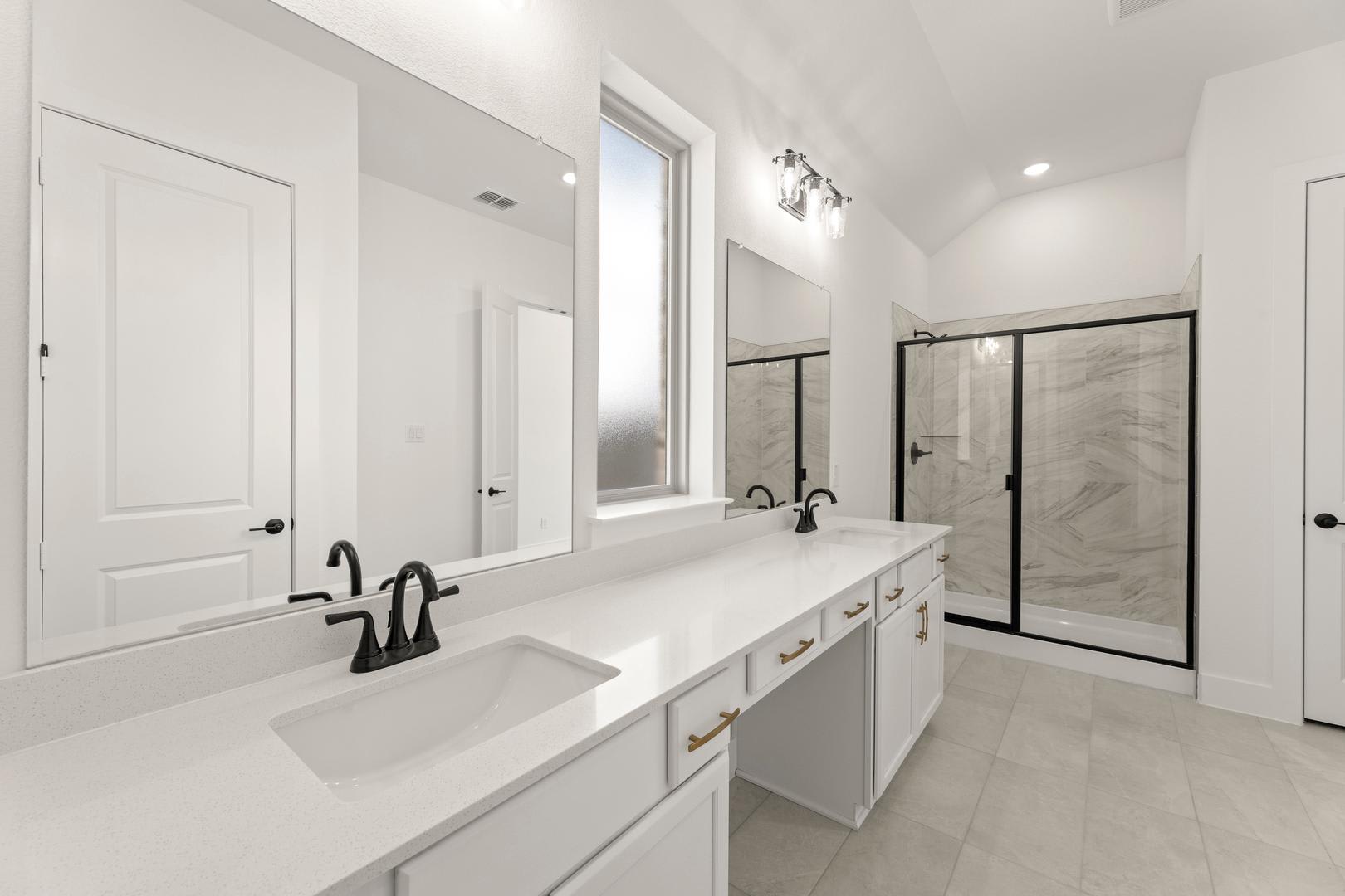 A modern, minimalist bathroom with a double vanity, white countertops, and a large mirror on the wall. The room has a clean, bright, and spacious feel.