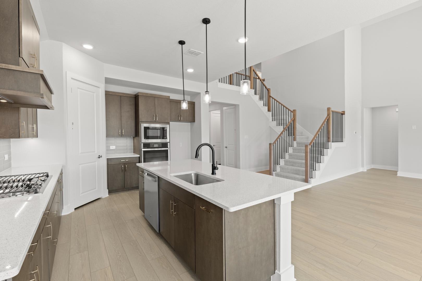 A modern, open-concept kitchen with a large island, stainless steel appliances, and a wooden staircase leading to the upper level in the background.