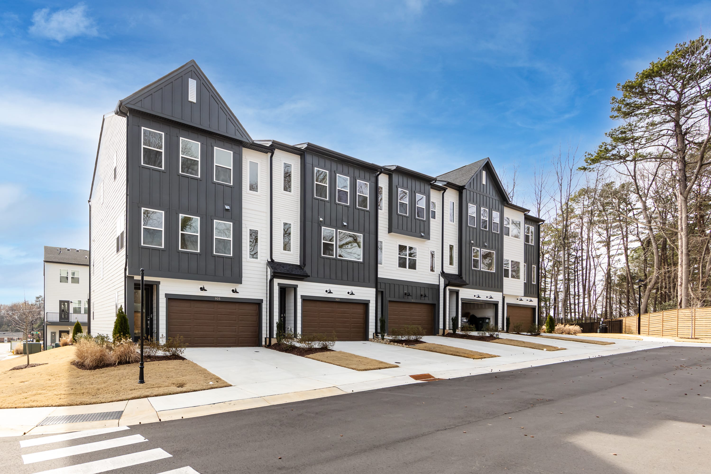 A modern multi-story townhouse complex with a gray exterior, surrounded by trees and a paved road in the foreground.