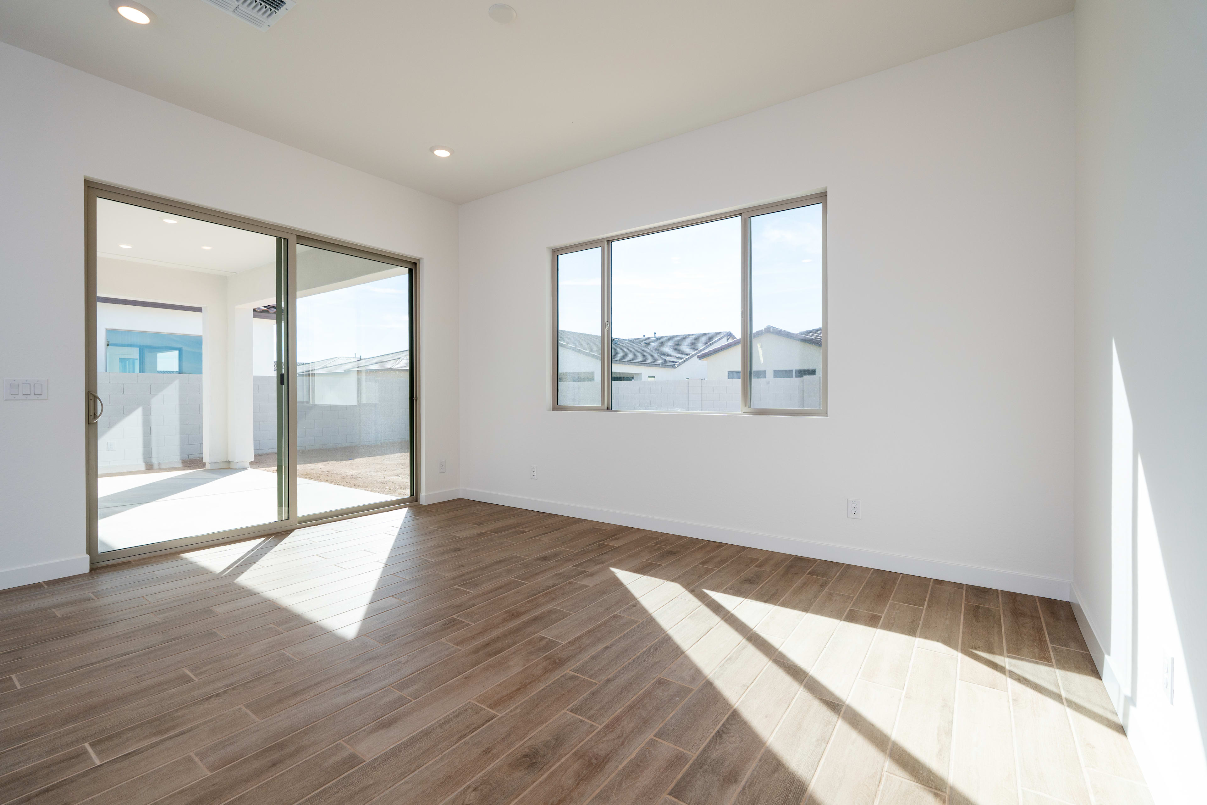 A bright and spacious room with wooden flooring, large windows, and a sliding glass door leading to an outdoor area.