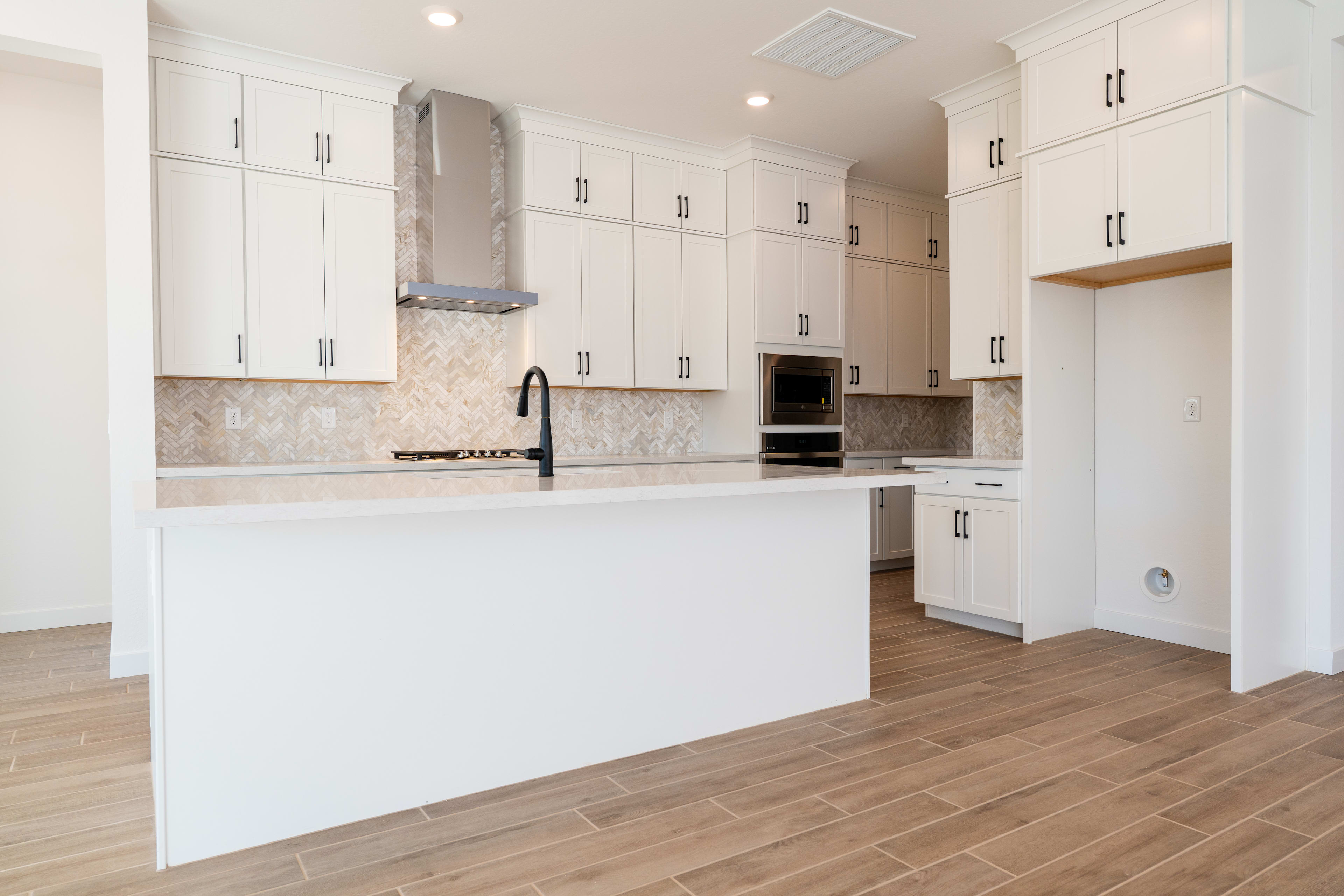 A modern, open-concept kitchen with white cabinets, a tile backsplash, and hardwood floors, creating a bright and spacious atmosphere.