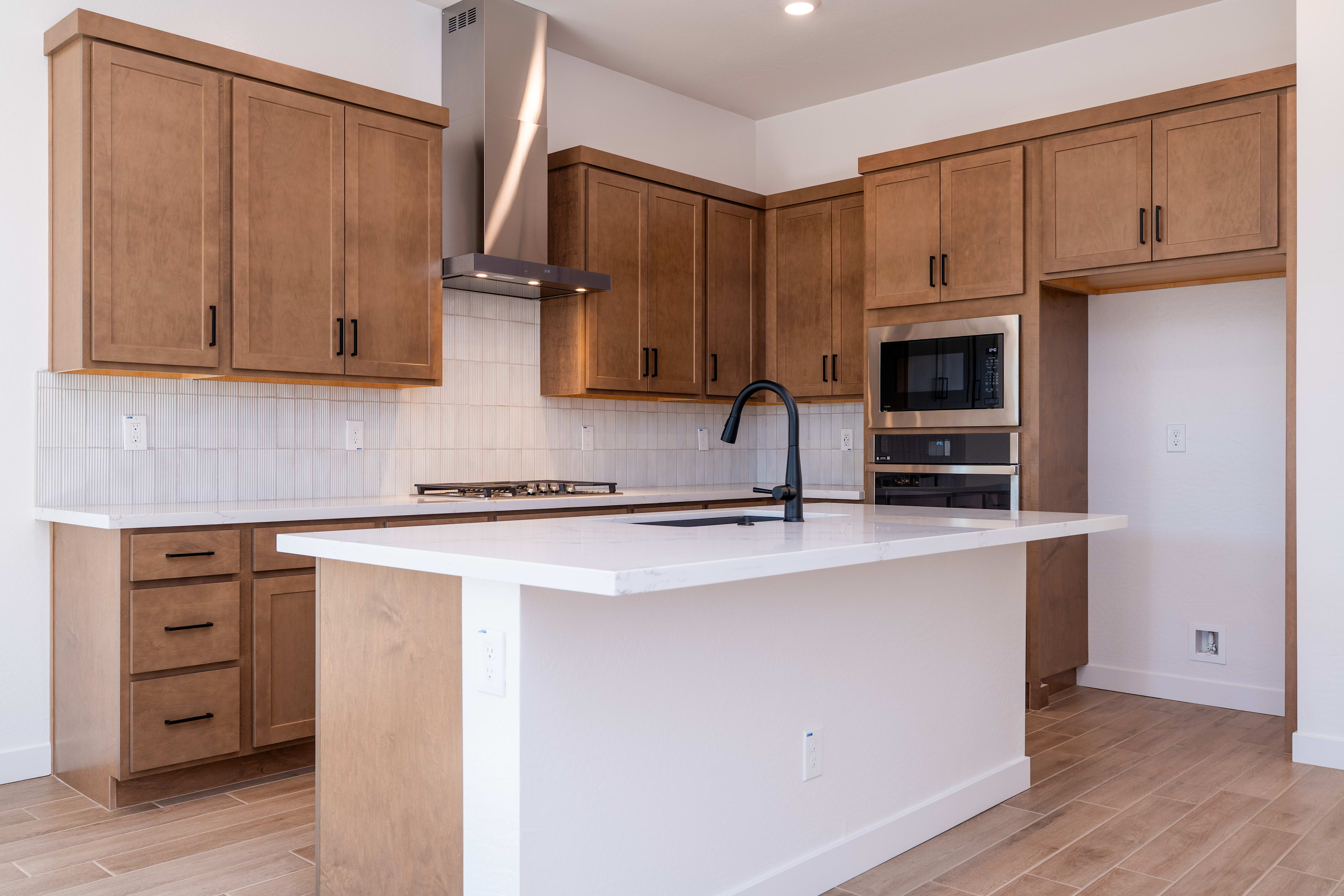A modern kitchen with wooden cabinets, a white countertop, and a stainless steel appliance in the background.