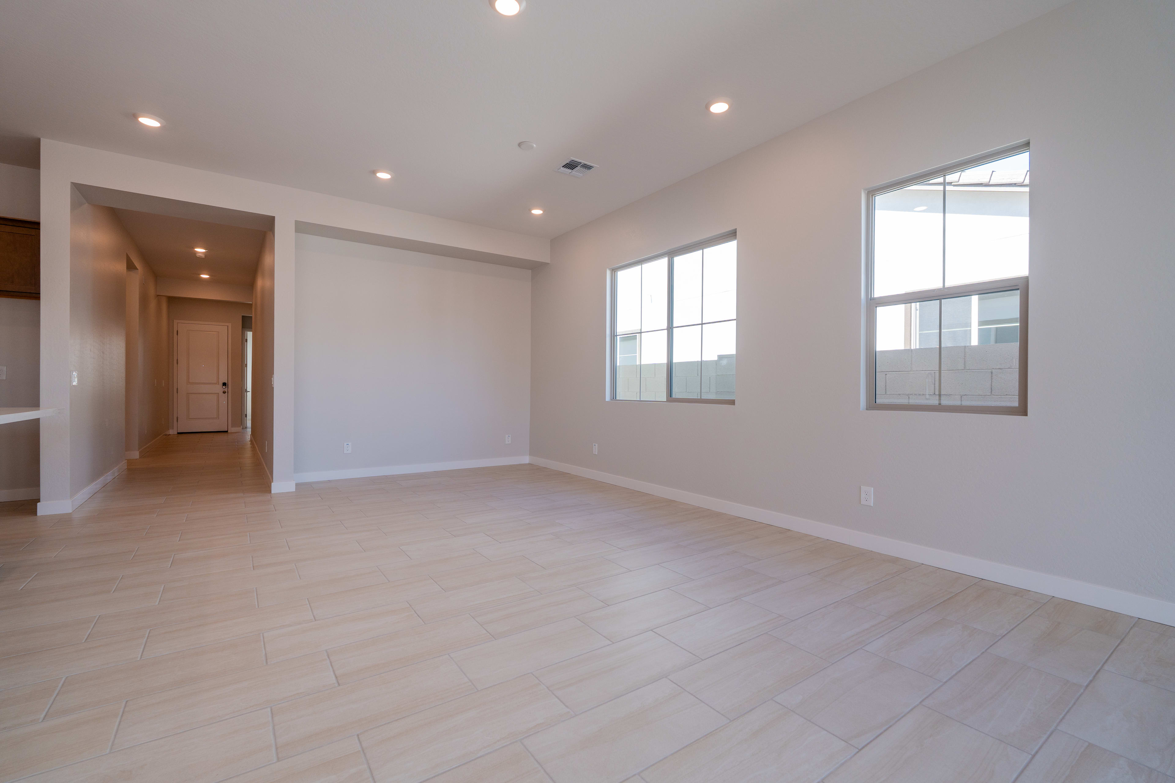 A spacious, well-lit room with a hardwood floor, recessed lighting, and large windows providing natural illumination.