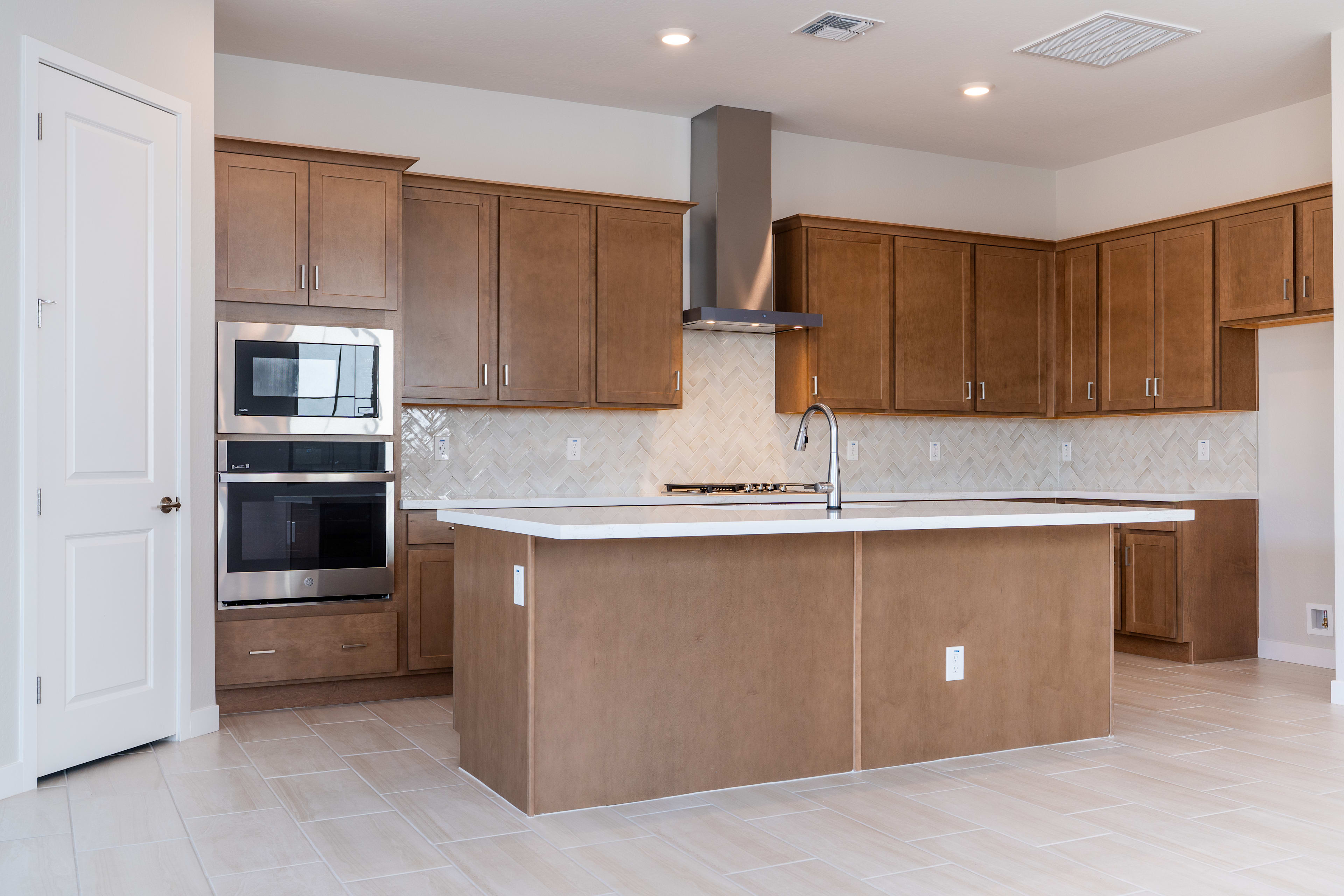 A modern kitchen with wooden cabinets, a white countertop, and stainless steel appliances, including a range hood and oven.