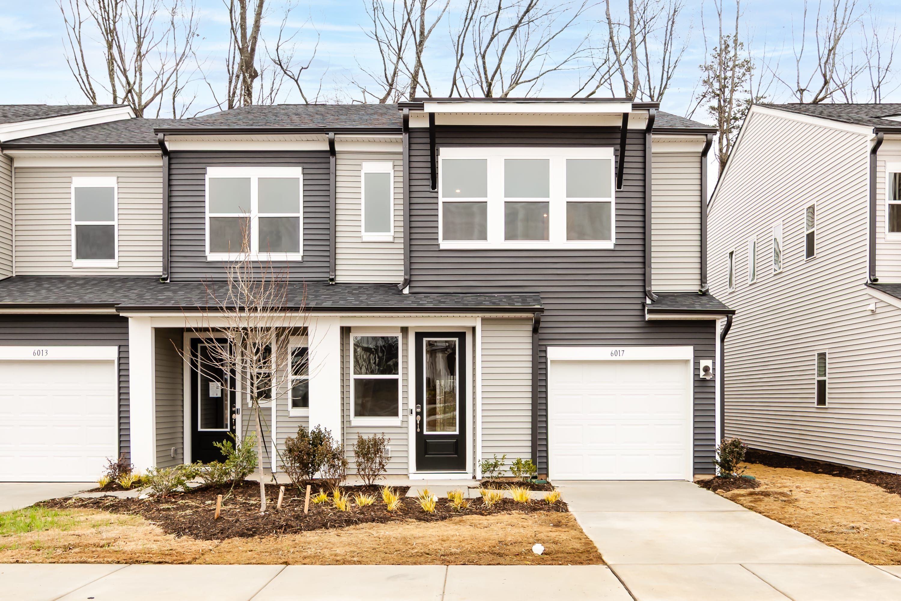 A two-story townhouse with a garage, surrounded by bare trees and a grassy yard in the foreground.
