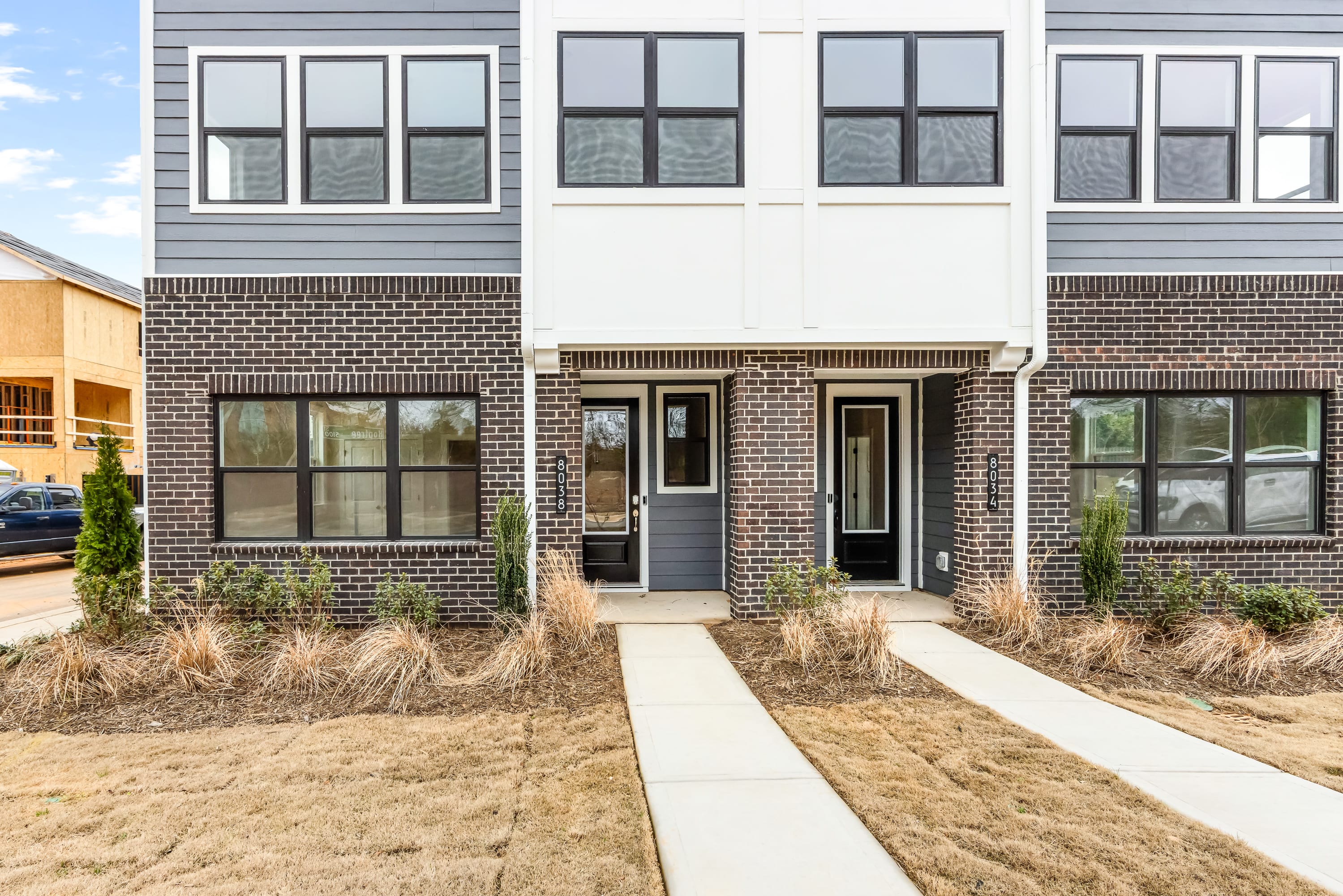 A modern townhouse with a brick exterior, surrounded by a grassy area and a paved walkway leading to the entrance.