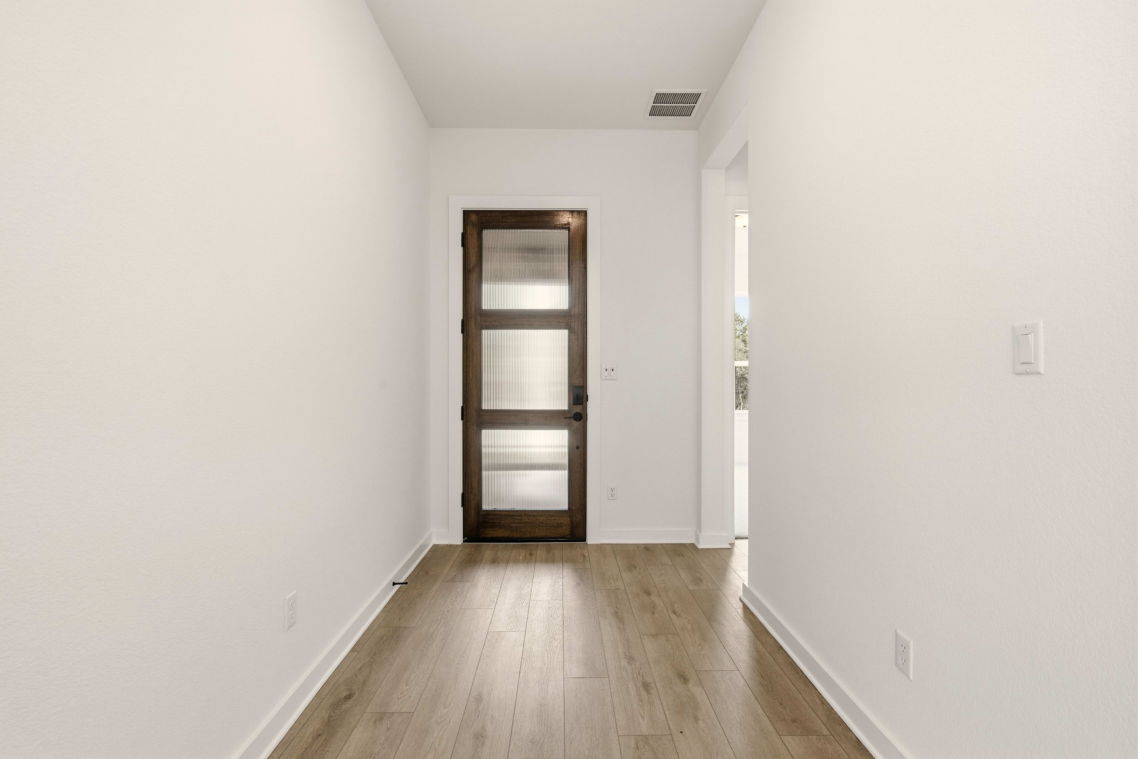 A simple, minimalist hallway with a wooden door frame and a hardwood floor leading to a bright, open space.