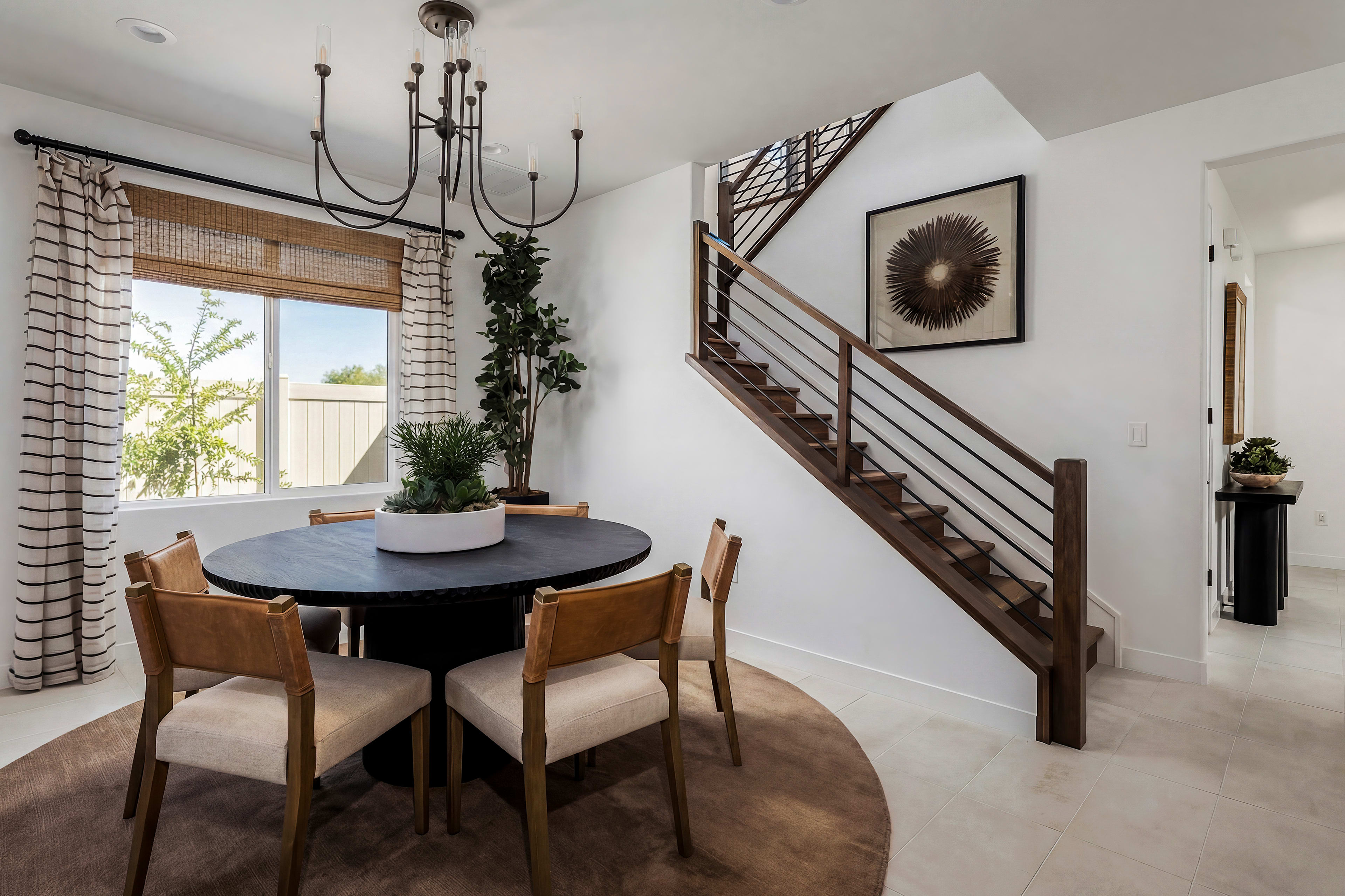 A cozy dining area with a round wooden table and chairs, surrounded by a staircase, curtains, and various decorative elements, creating a warm and inviting atmosphere.
