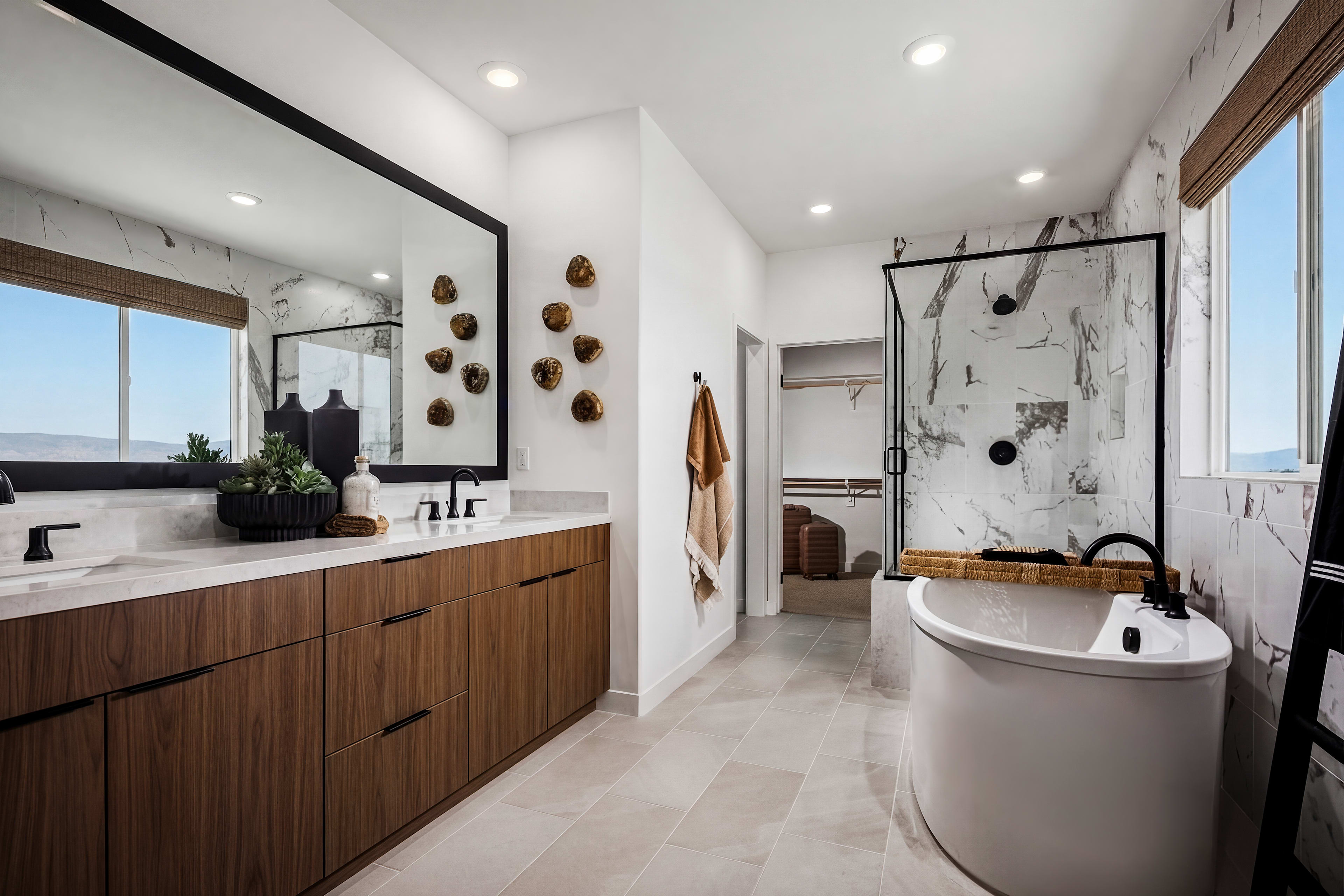 A modern and stylish bathroom with a wooden vanity, a freestanding bathtub, and decorative wall accents, set against a backdrop of large windows offering a scenic view.
