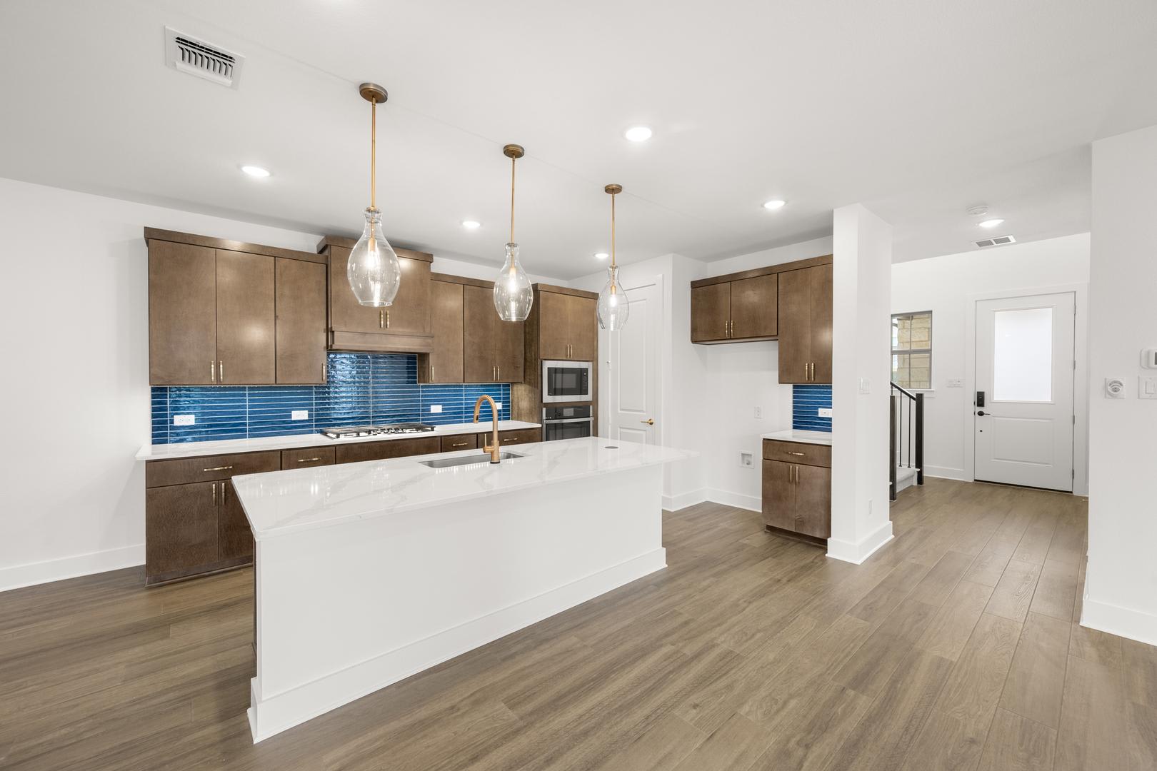 A modern and spacious kitchen with wooden cabinets, a white island, and pendant lights hanging from the ceiling, set against a backdrop of hardwood floors.