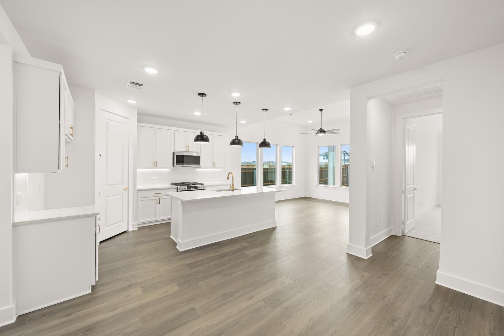 A modern, open-concept kitchen with white cabinets, hardwood floors, and pendant lighting, leading into a bright and airy living space.