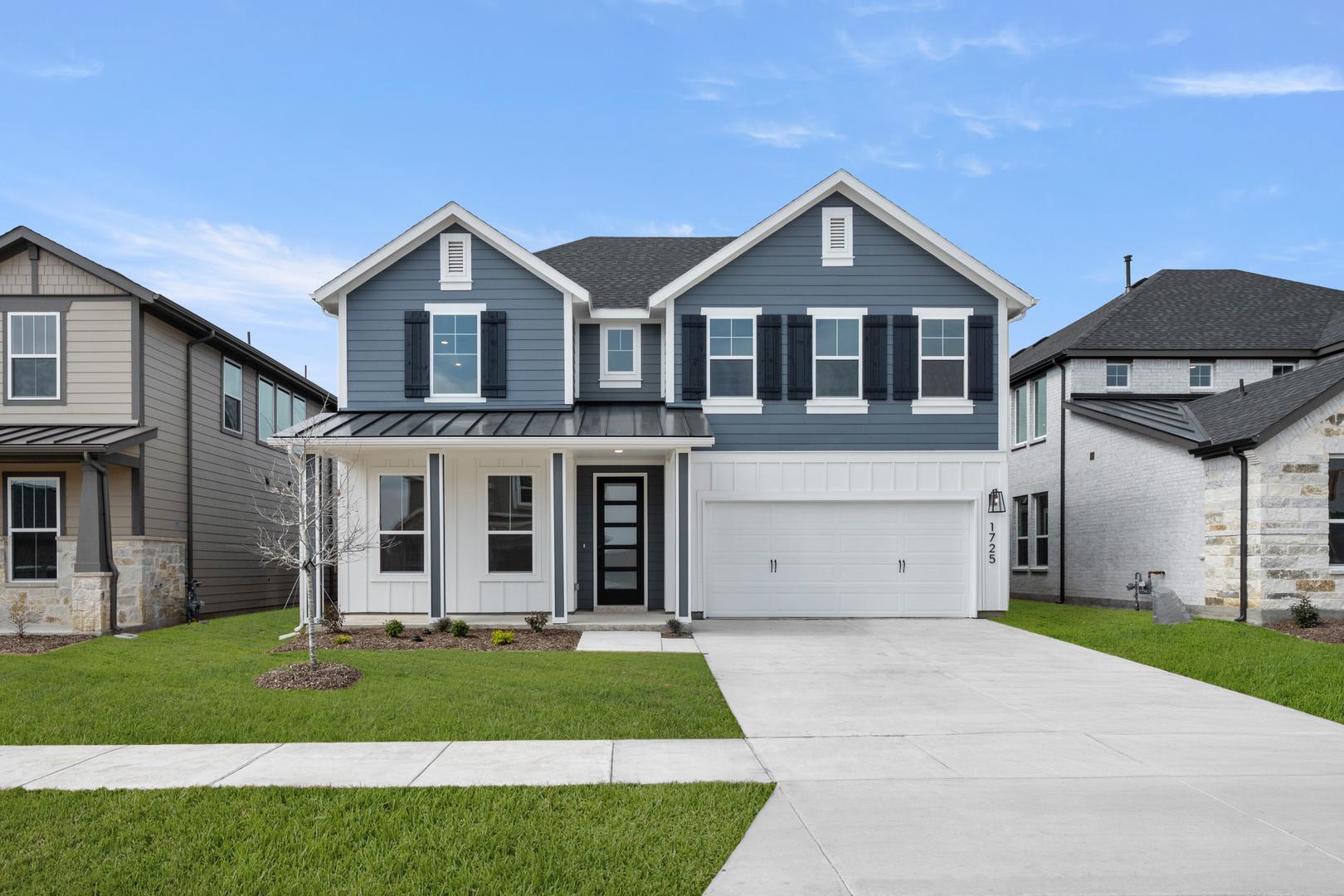 A two-story gray house with a garage, surrounded by a well-manicured lawn and set against a clear blue sky with scattered clouds.