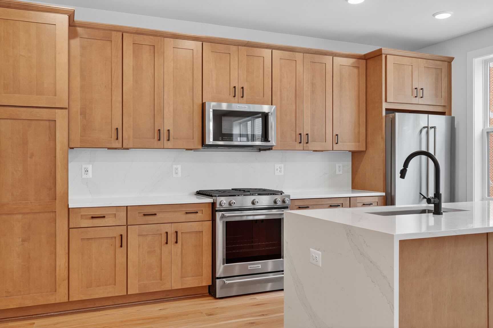 A modern kitchen with light wood cabinets, stainless steel appliances, and a white countertop.