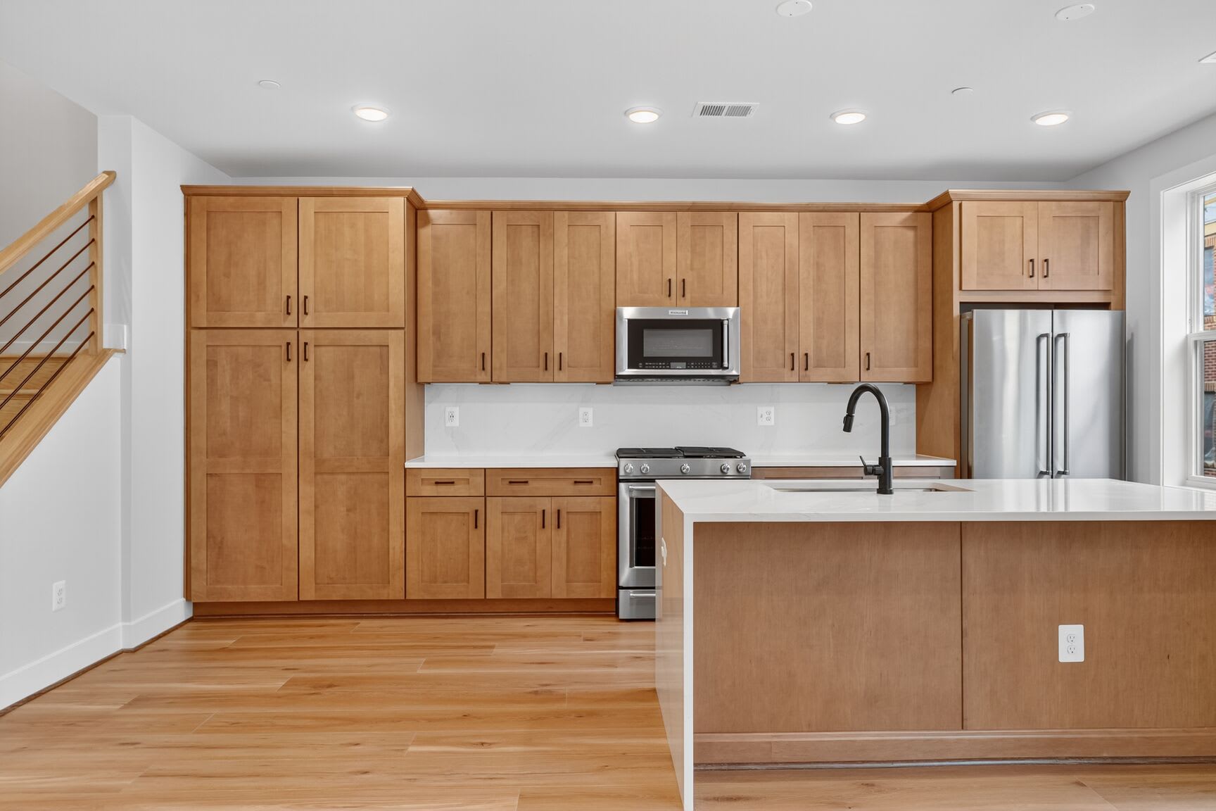 A modern kitchen with light wood cabinets, stainless steel appliances, and a central island with a white countertop.
